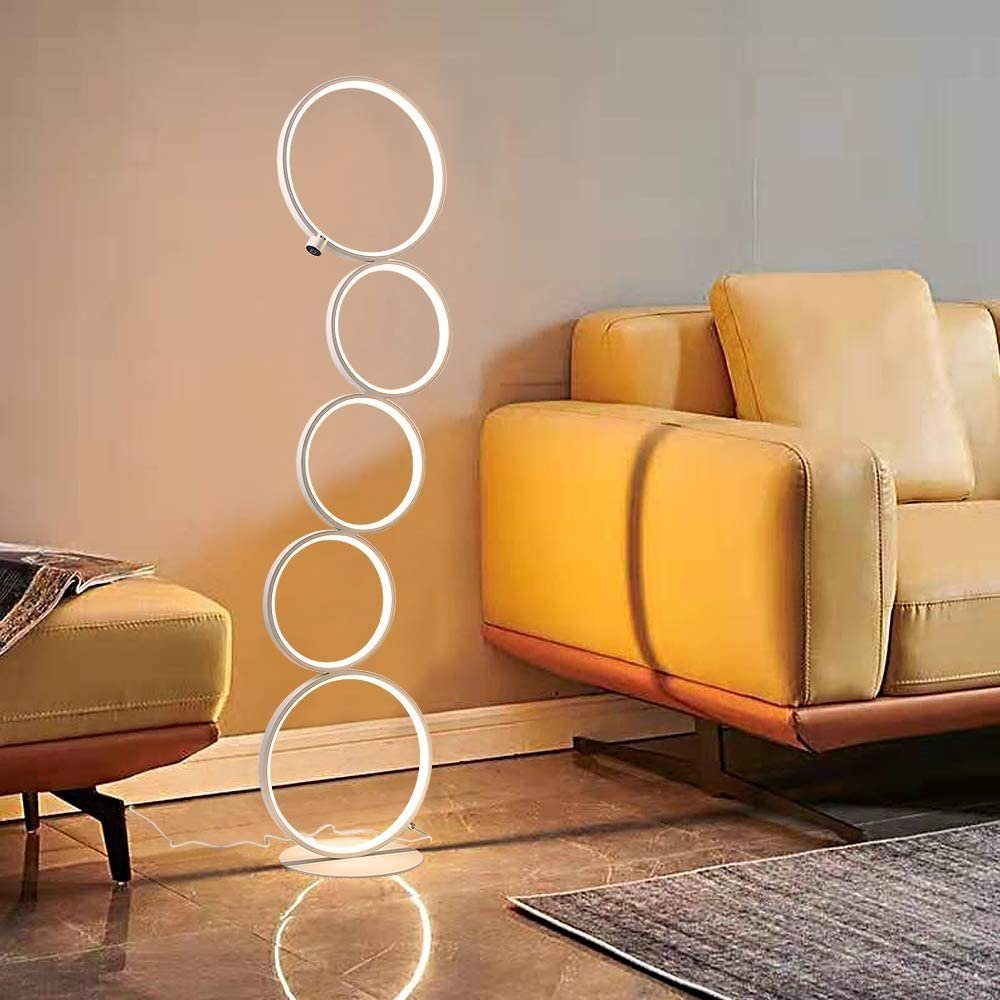 Modernes Wohnzimmer mit einzigartiger Stehlampe mit beleuchteten Ringen. Ein gelbes Sofa und ein Hocker sind sichtbar.