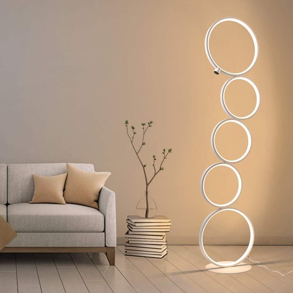 Ein modernes Wohnzimmer mit grauem Sofa, Kissen, Bücherstapel, Pflanze und einer einzigartigen Kreisförmigen Lampe.