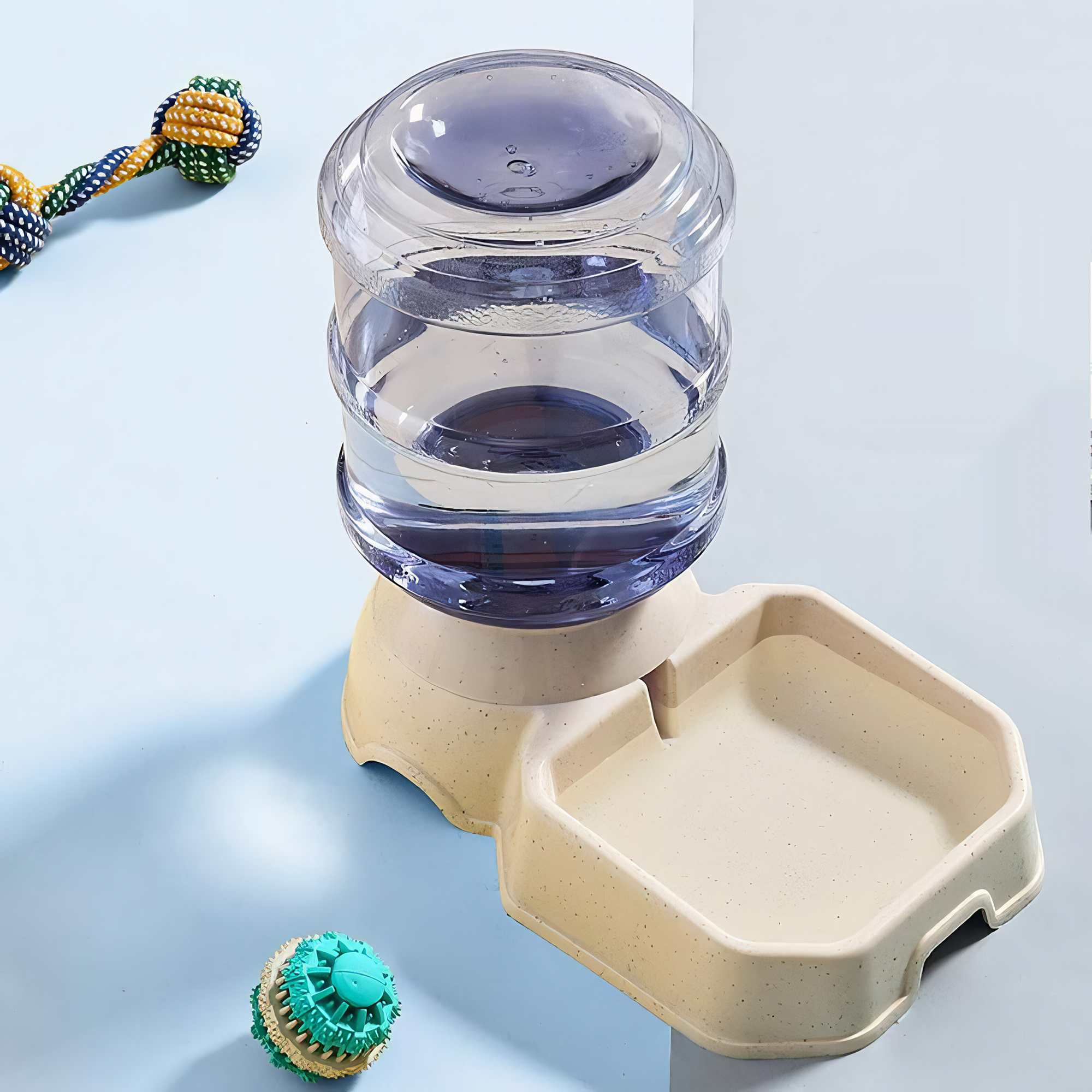 Ein Wasserspender für Haustiere mit Wasserbehälter und Futternapf. Spielzeug wie ein Seil und ein Ball liegen daneben.