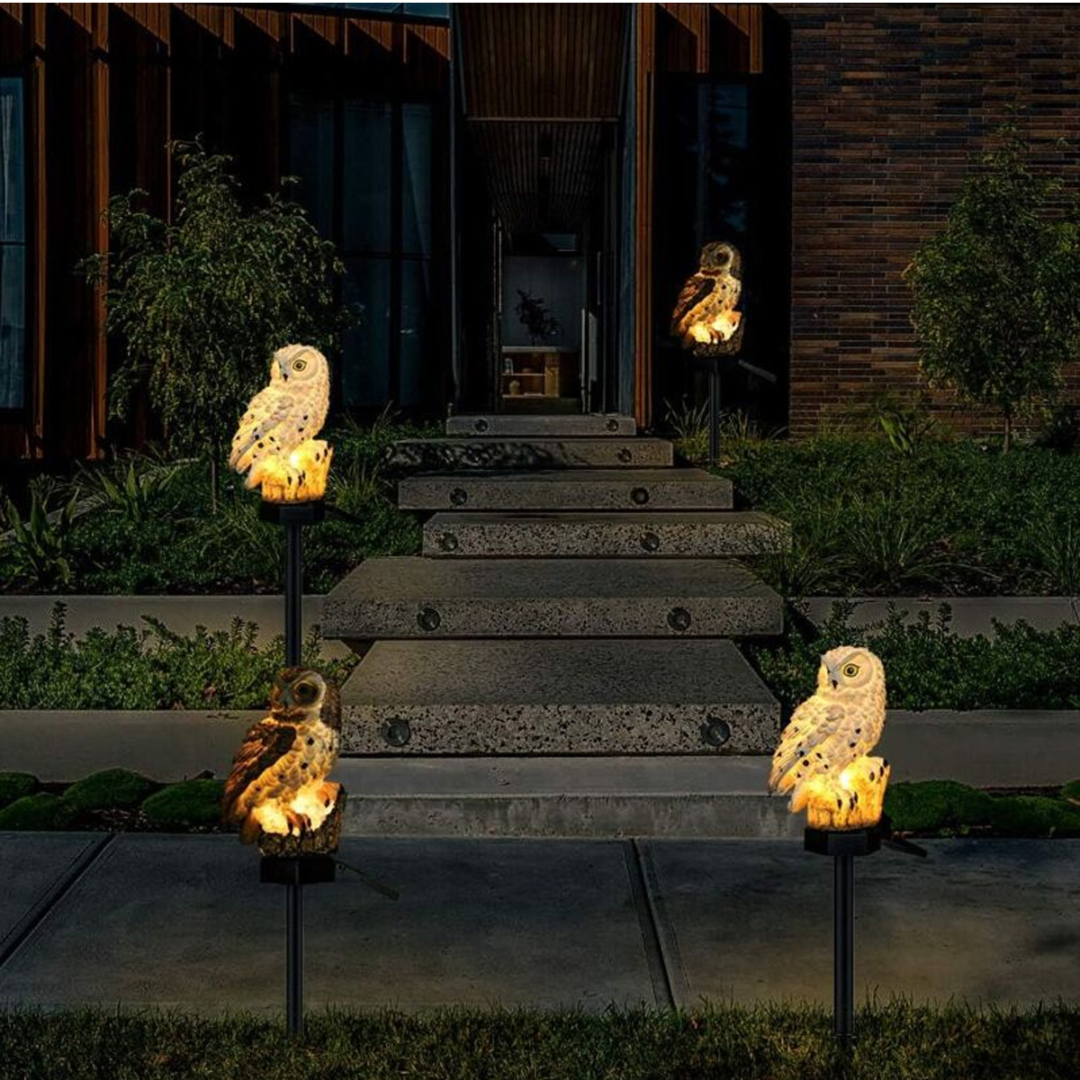 Eine Außenszene mit eulenartigen Lichtern, die einen Weg zu einem Haus beleuchten. Die Lichter stehen auf Pfählen und erzeugen ein warmes Ambiente.
