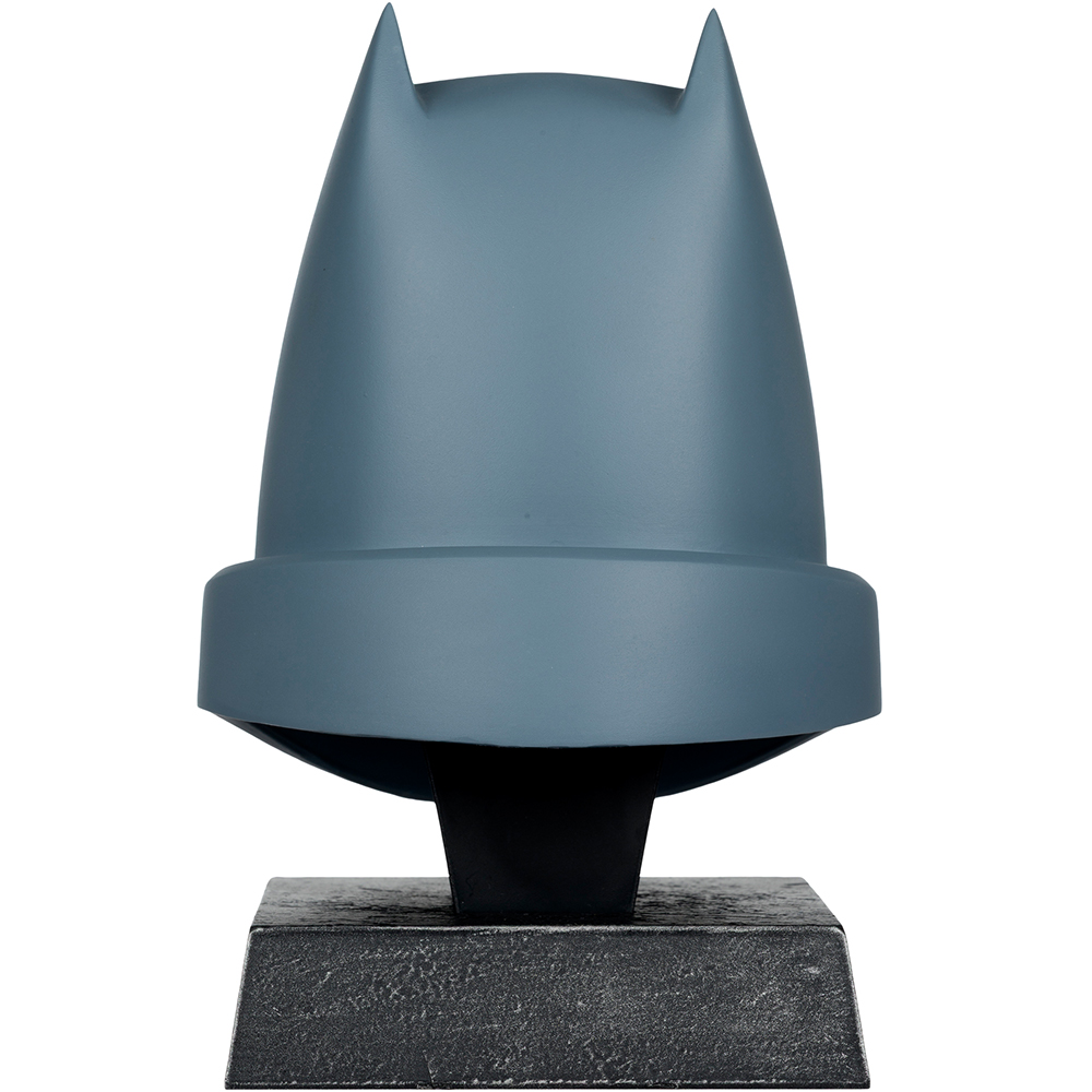 Una statua a forma di casco di Batman grigio, con orecchie a punta, montata su un supporto nero. La base è un blocco grigio strutturato.