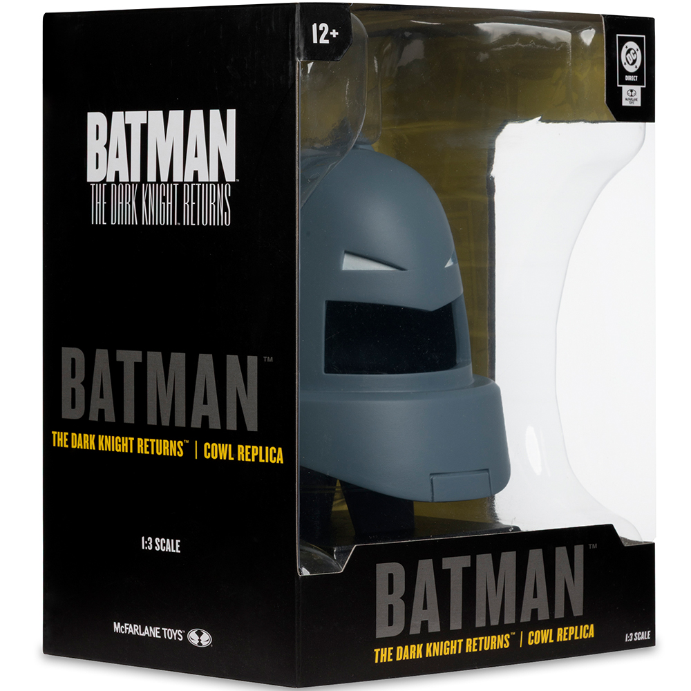 Una replica del cappuccio di Batman in una scatola. La scatola è nera con il marchio Batman e una finestra trasparente che mostra il cappuccio grigio.