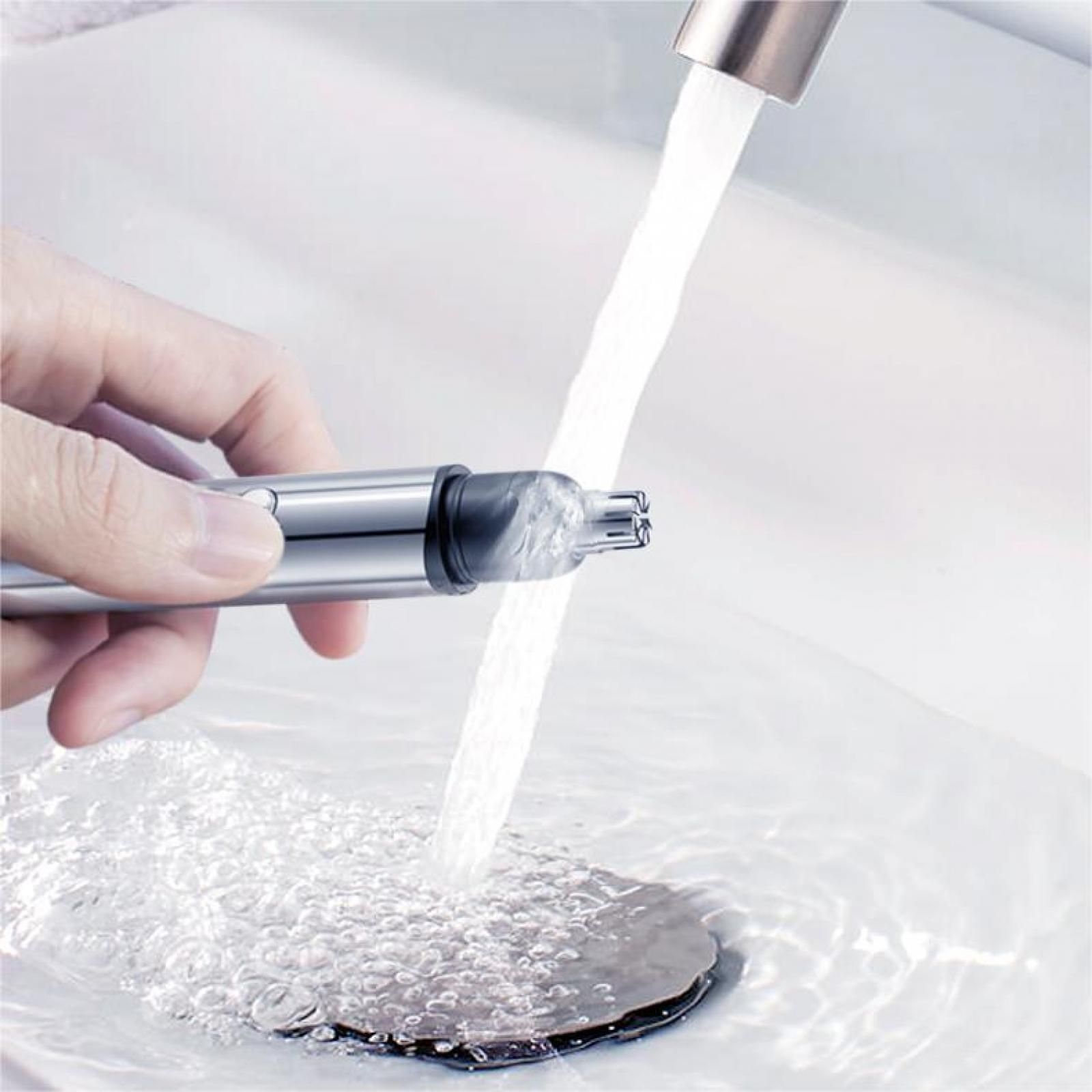 Ein silberner Nasenhaartrimmer, der unter fließendem Wasser in einem weißen Waschbecken gewaschen wird. Hand, die das Gerät hält.