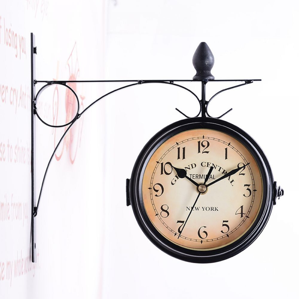 Doppelseitige Uhr, schwarzer Rahmen mit beigefarbenem Zifferblatt. Liest 'Grand Central Terminal, New York'. An einer weißen Wand mit schwarzem Metallträger montiert.