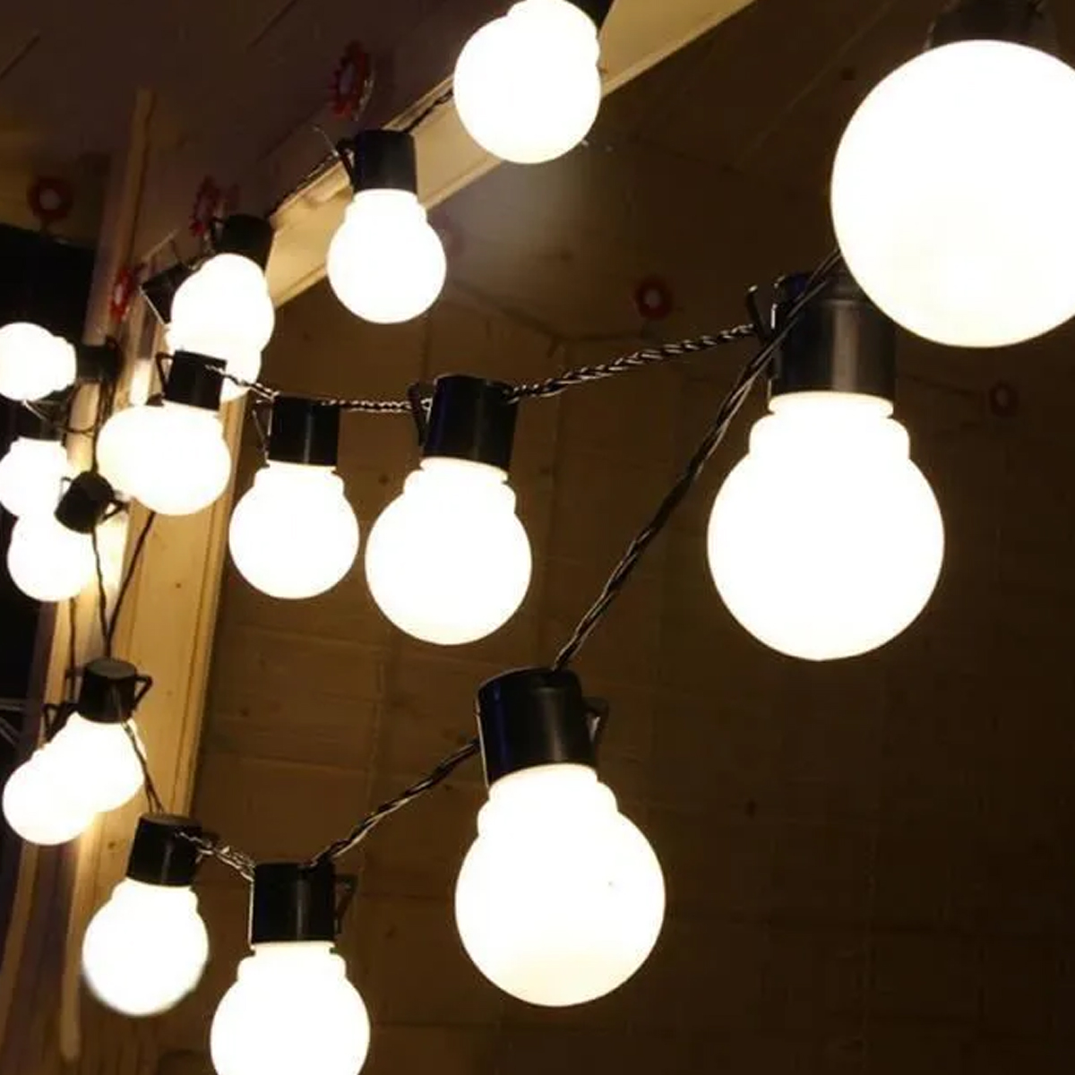 Lichterketten mit runden, weißen Glühbirnen hängen vor einem dunklen Holzhintergrund. Die Glühbirnen leuchten und erzeugen ein warmes Leuchten.
