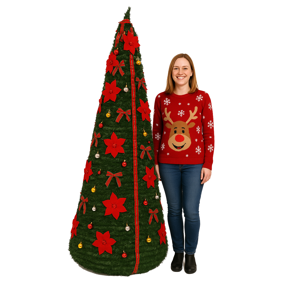 Una mujer está de pie junto a un árbol de Navidad decorado. Lleva un suéter rojo con un diseño de reno y vaqueros azules.