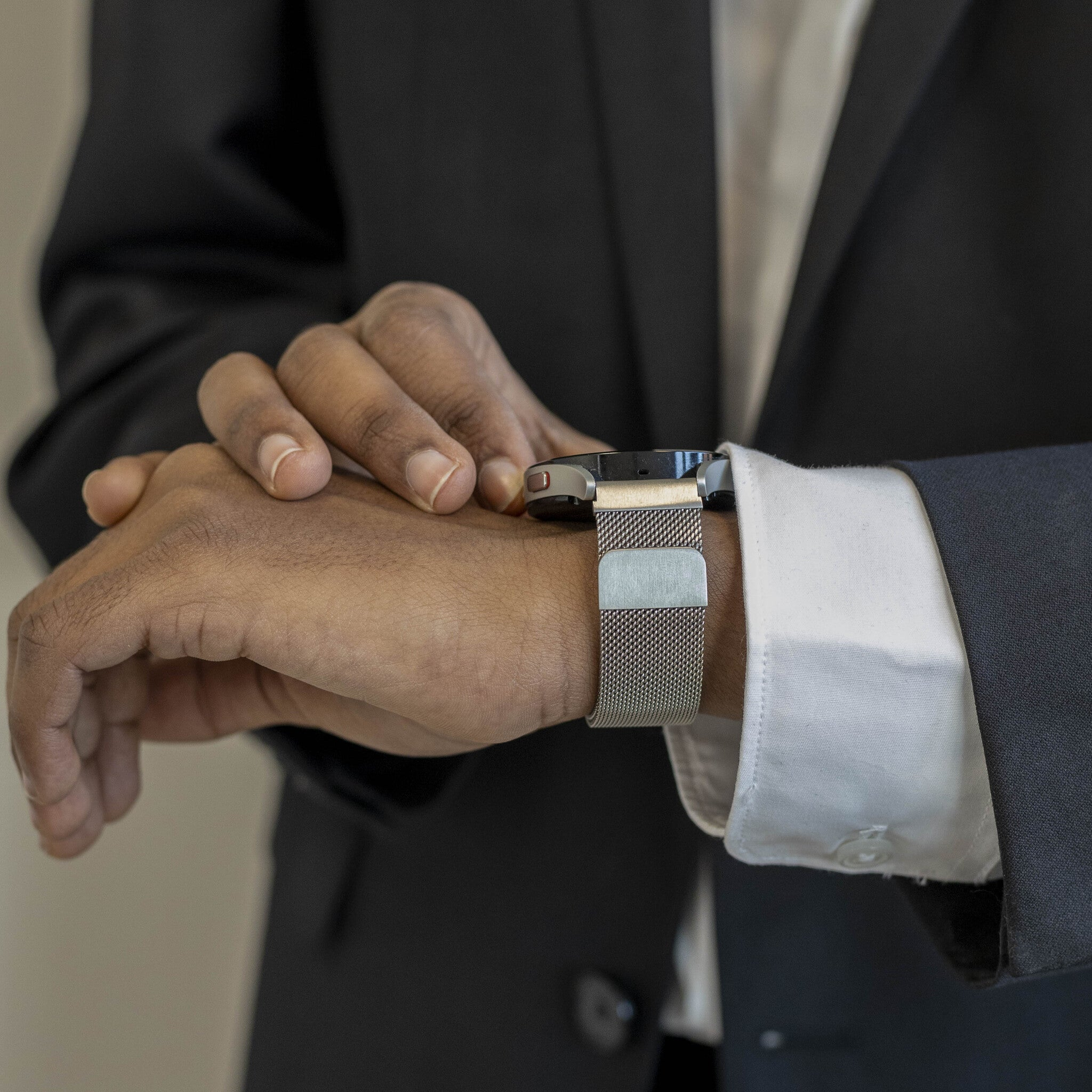 Eine Person im Anzug stellt die Armbanduhr ein. Die Uhr hat ein Metallband. Die Haut der Person ist braun.