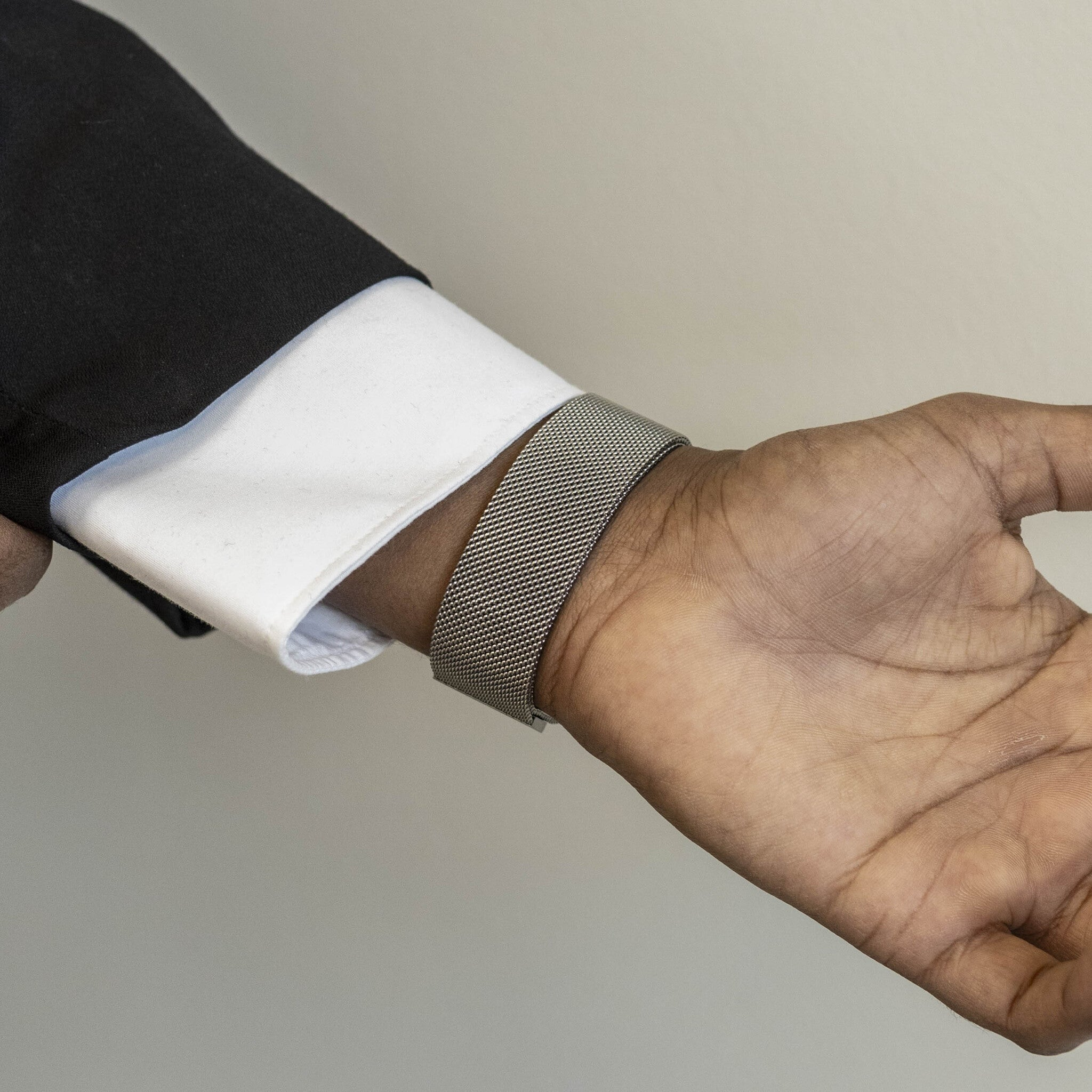 Nahaufnahme eines Arms. Am Handgelenk befindet sich eine silberne Uhr. Ein weißes Hemd und ein schwarzer Anzug sind zu sehen.