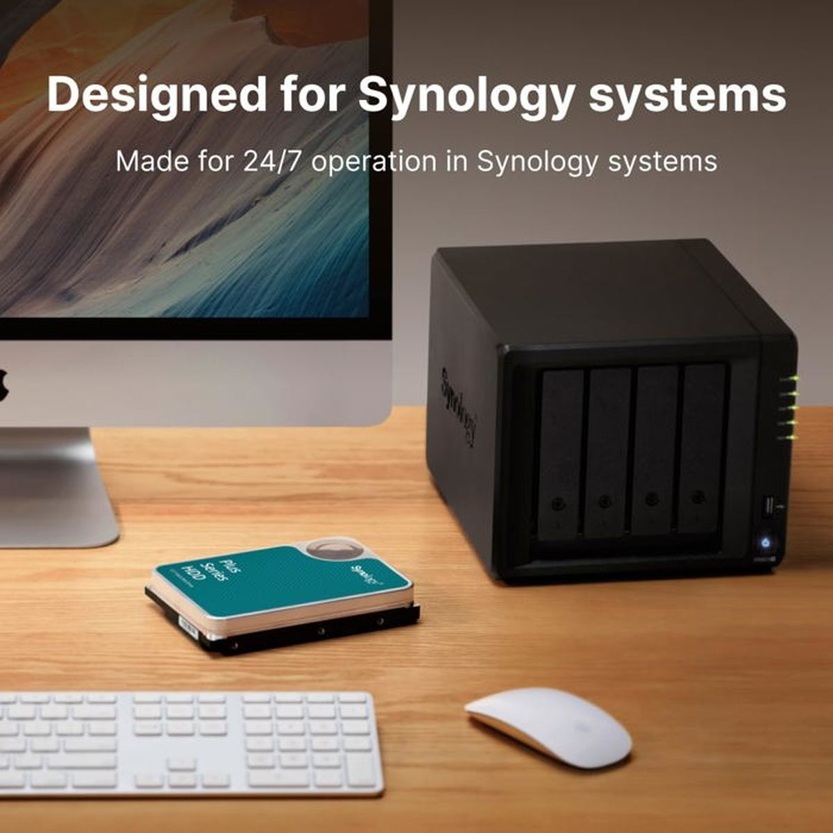 Un dispositivo NAS Synology nero è su una scrivania di legno, accanto a un monitor, tastiera, mouse e un disco rigido.