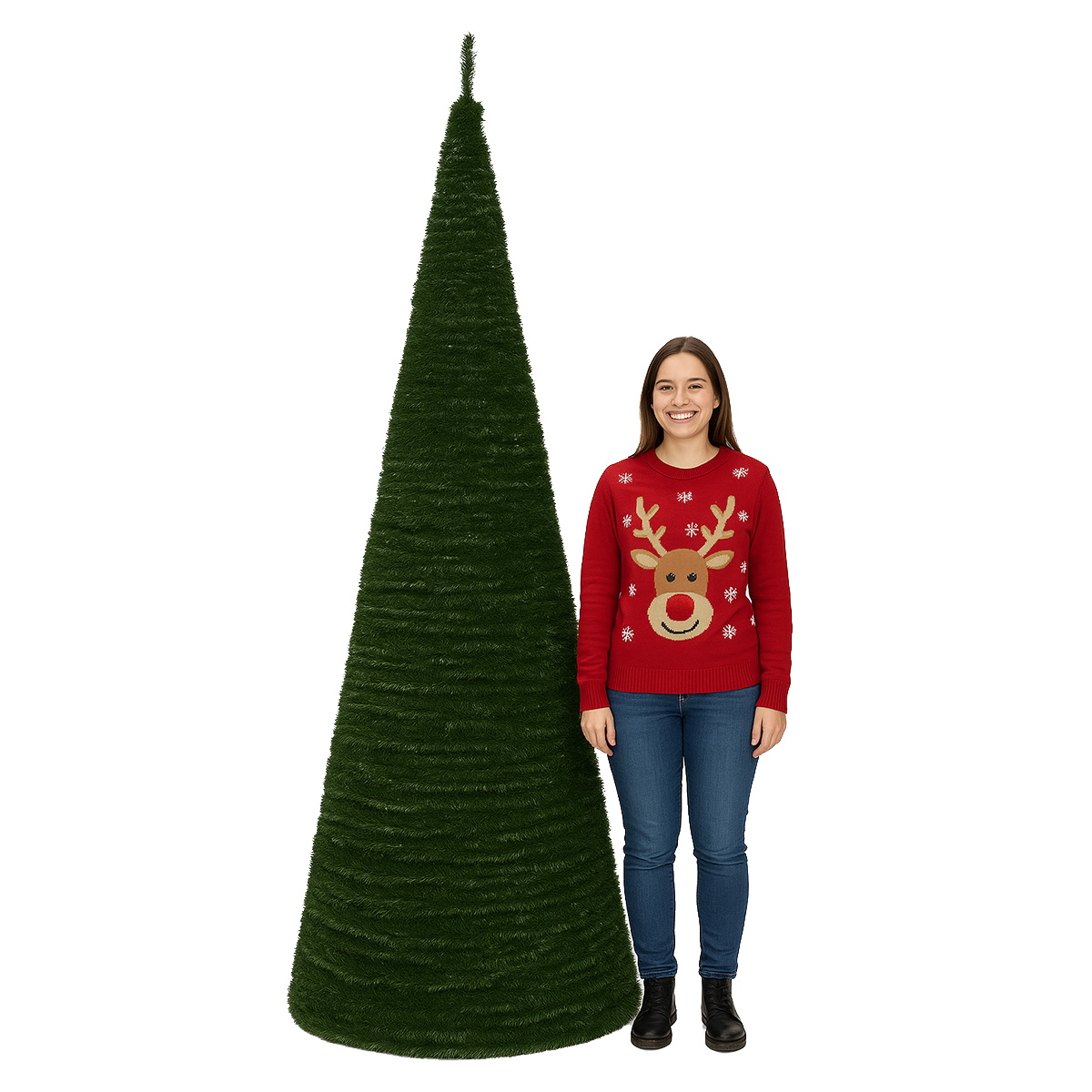 Una mujer con un suéter rojo de reno está de pie junto a un árbol de Navidad cónico verde alto sobre un fondo blanco.