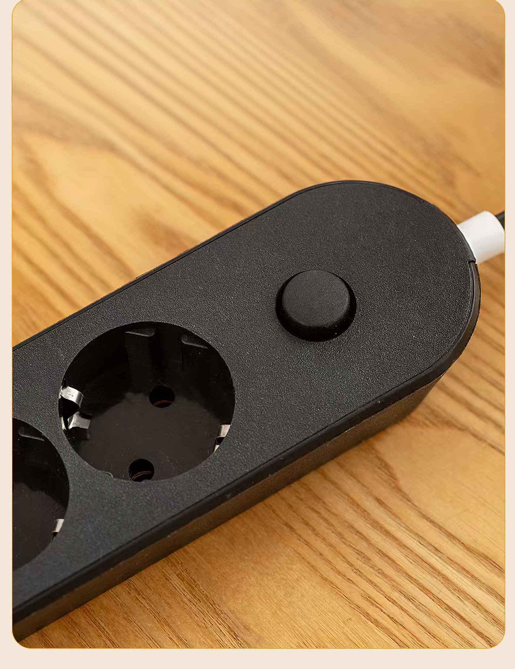 Nahaufnahme einer schwarzen Steckdosenleiste mit drei Steckdosen und einem Knopf auf Holz. Ein weißes Kabel ist eingesteckt.