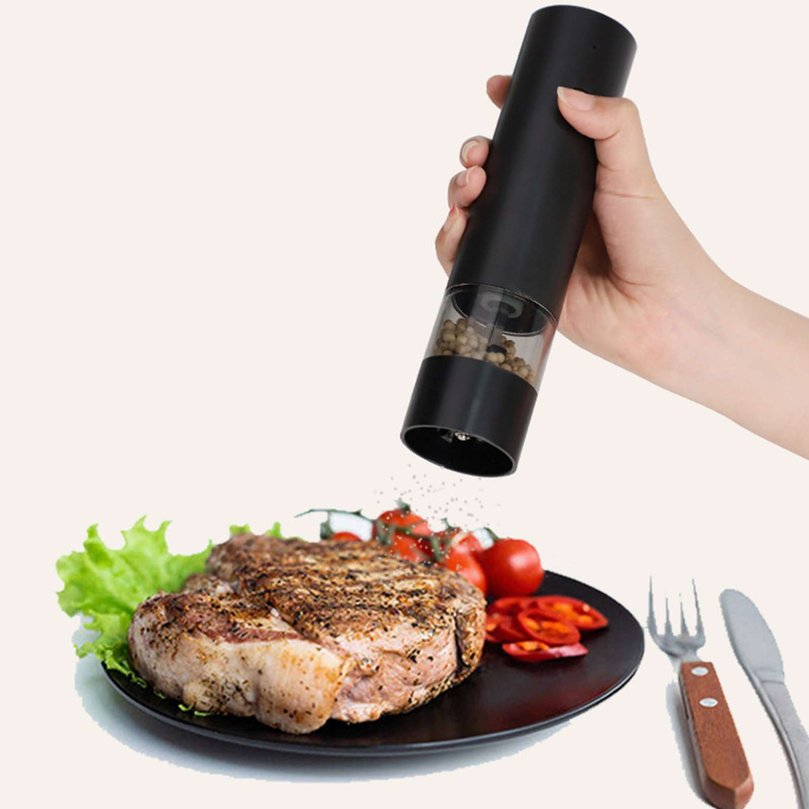 Eine Hand hält einen schwarzen Pfeffermühle über einem Steak auf einem Teller mit Tomaten und Salat. Pfeffer wird abgegeben.