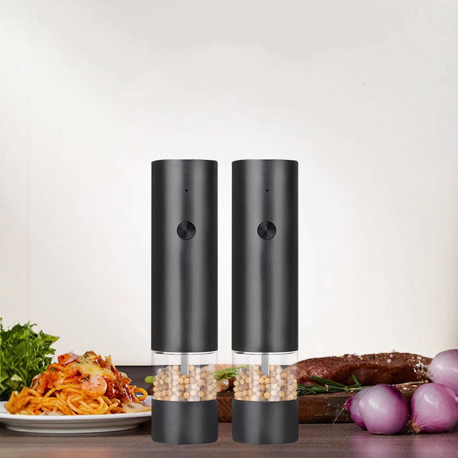 Zwei schwarze elektrische Pfeffermühlen. Spaghetti, Fleisch und Zwiebeln stehen auf einem Holztisch.