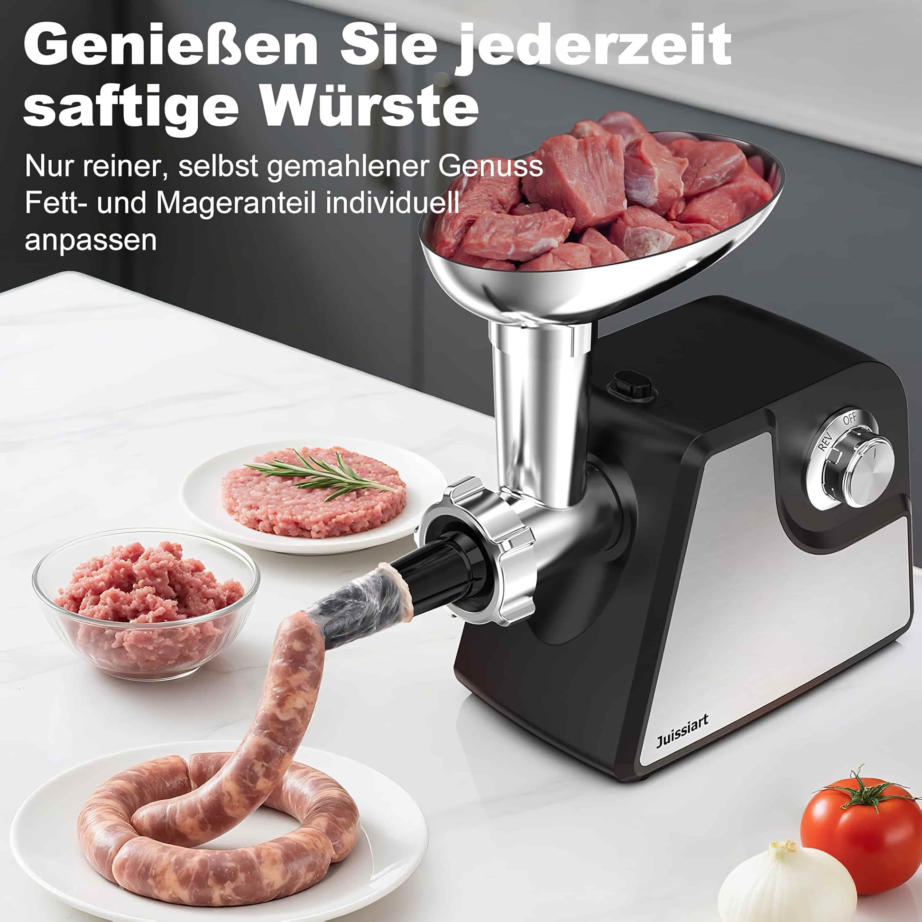 Ein Fleischwolf zerkleinert Fleisch zu Wurst. Rohes Fleisch, Wurst, Tomaten und Zwiebeln liegen auf weißem Grund.