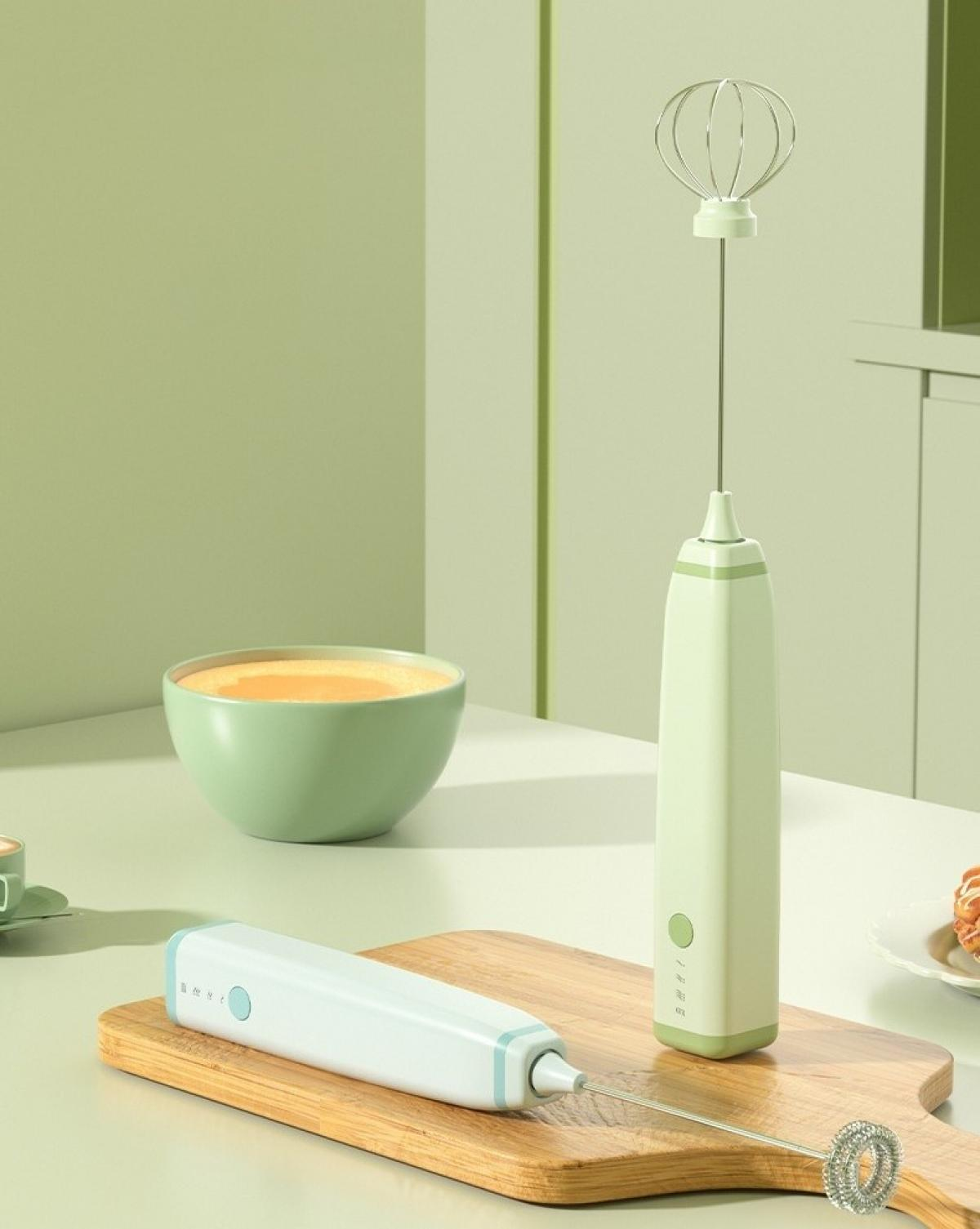 Eine Küchenszene mit einem Handmixer, einer Schüssel mit Essen und einem Holzschneidebrett. Der Mixer ist weiß und grün.