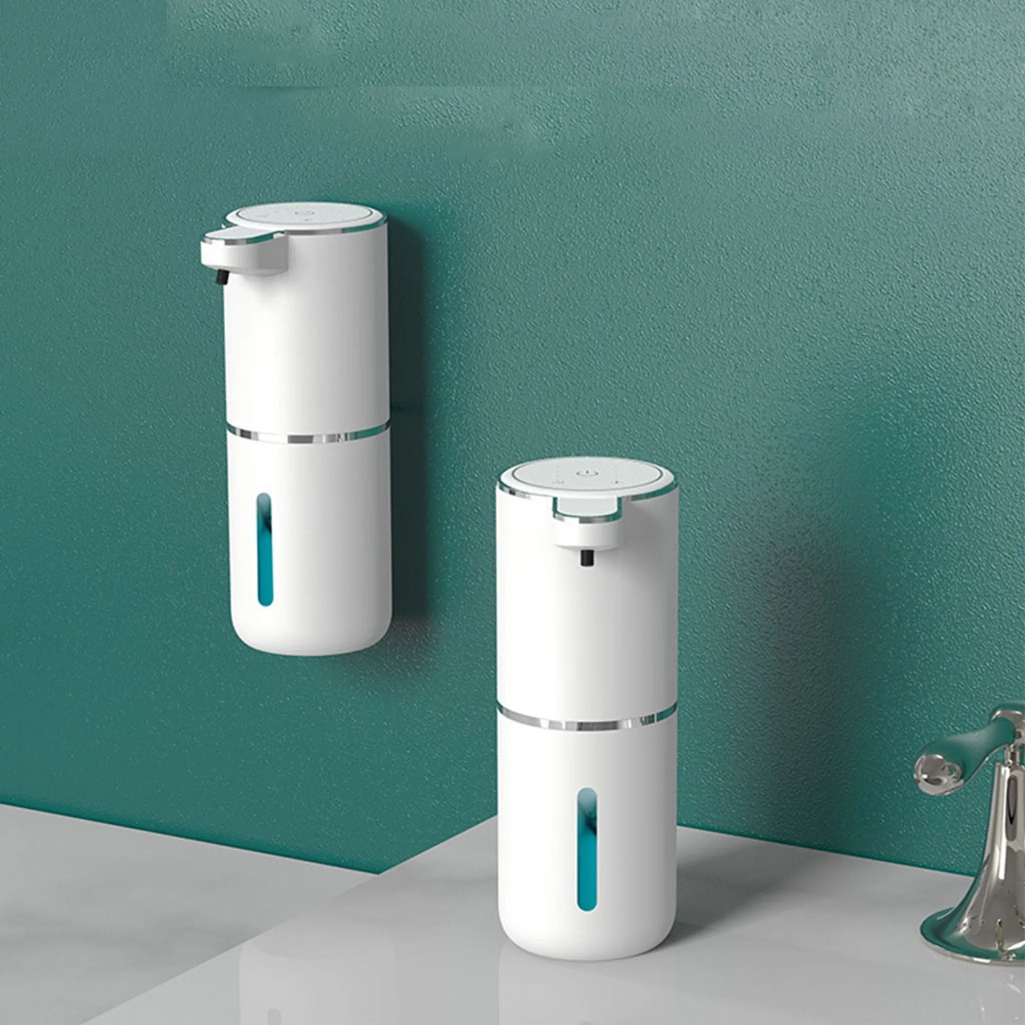 Zwei weiße automatische Seifenspender sind an einer tealfarbenen Wand angebracht. Ein Wasserhahn aus Chrom ist sichtbar.
