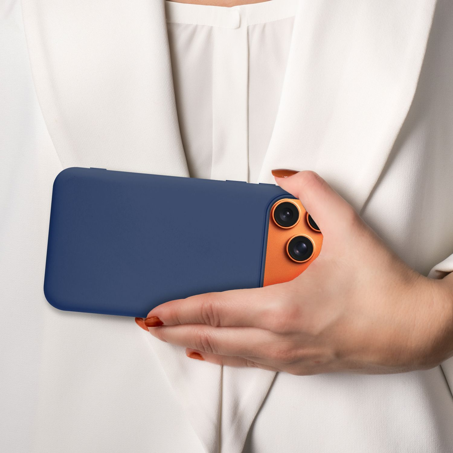 Eine Person hält ein marineblaues Telefon mit orangefarbener Kameralinse. Die Person trägt einen weißen Blazer. Die Nägel sind orange lackiert.