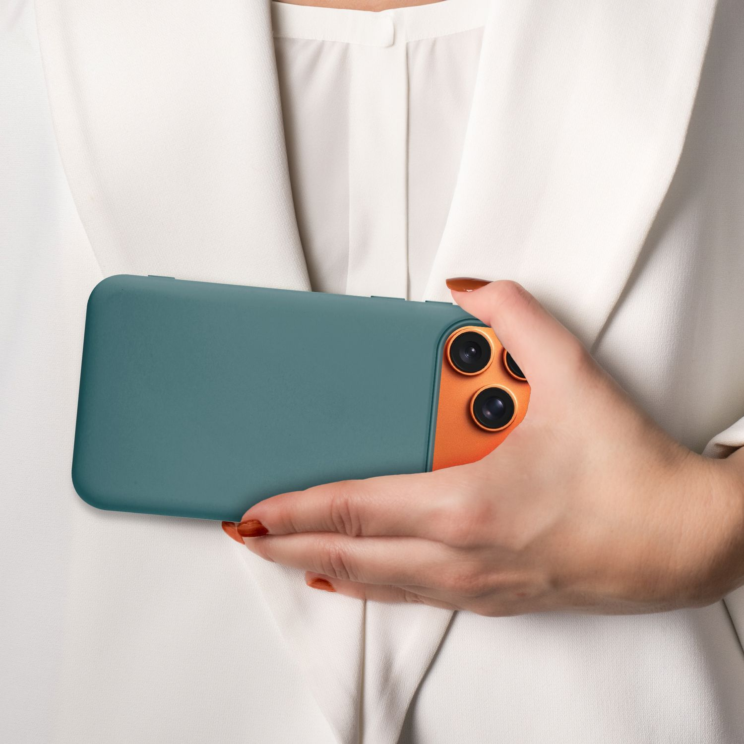 Eine Person hält ein türkisfarbenes Telefon. Das Telefon hat ein oranges Kameragehäuse. Die Person trägt einen weißen Blazer. Ihre Nägel sind orange lackiert.