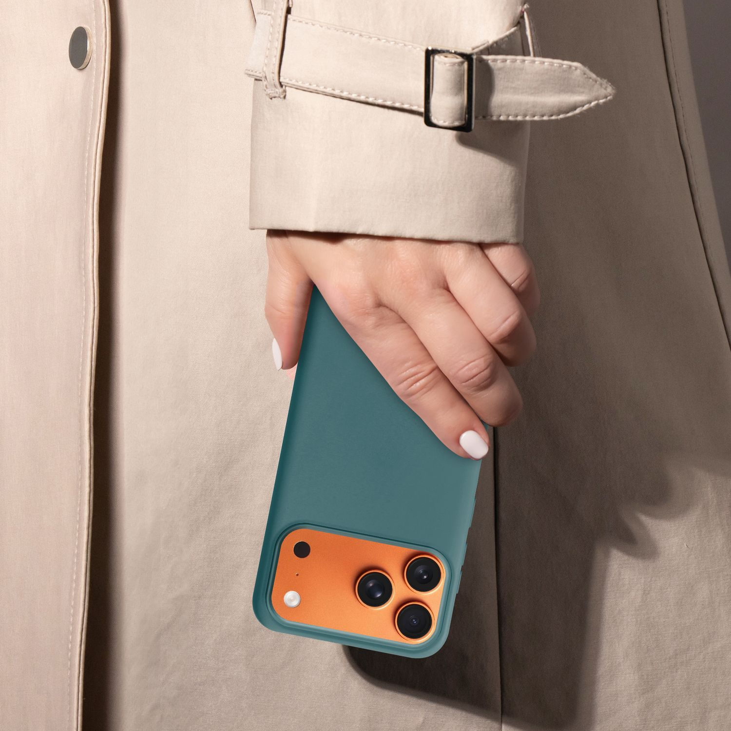 Hand hält eine tealfarbene Handyhülle vor einem beigen Mantel. Der Kamerabereich des Telefons ist orange. Nagellack ist weiß.