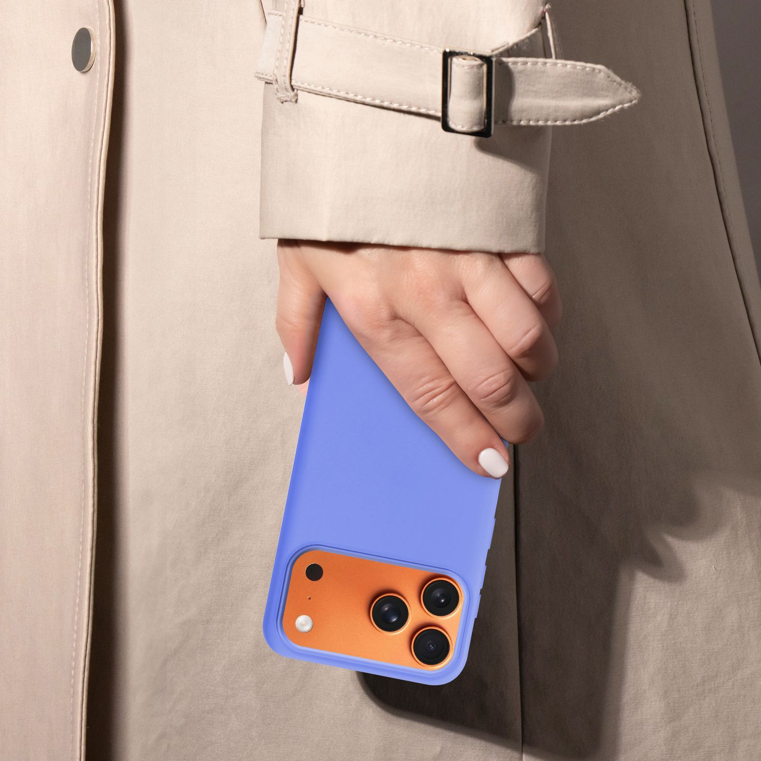 Eine Hand hält eine blaue Handyhülle mit orangefarbenem Kamerabereich. Die Person trägt einen beigefarbenen Trenchcoat.