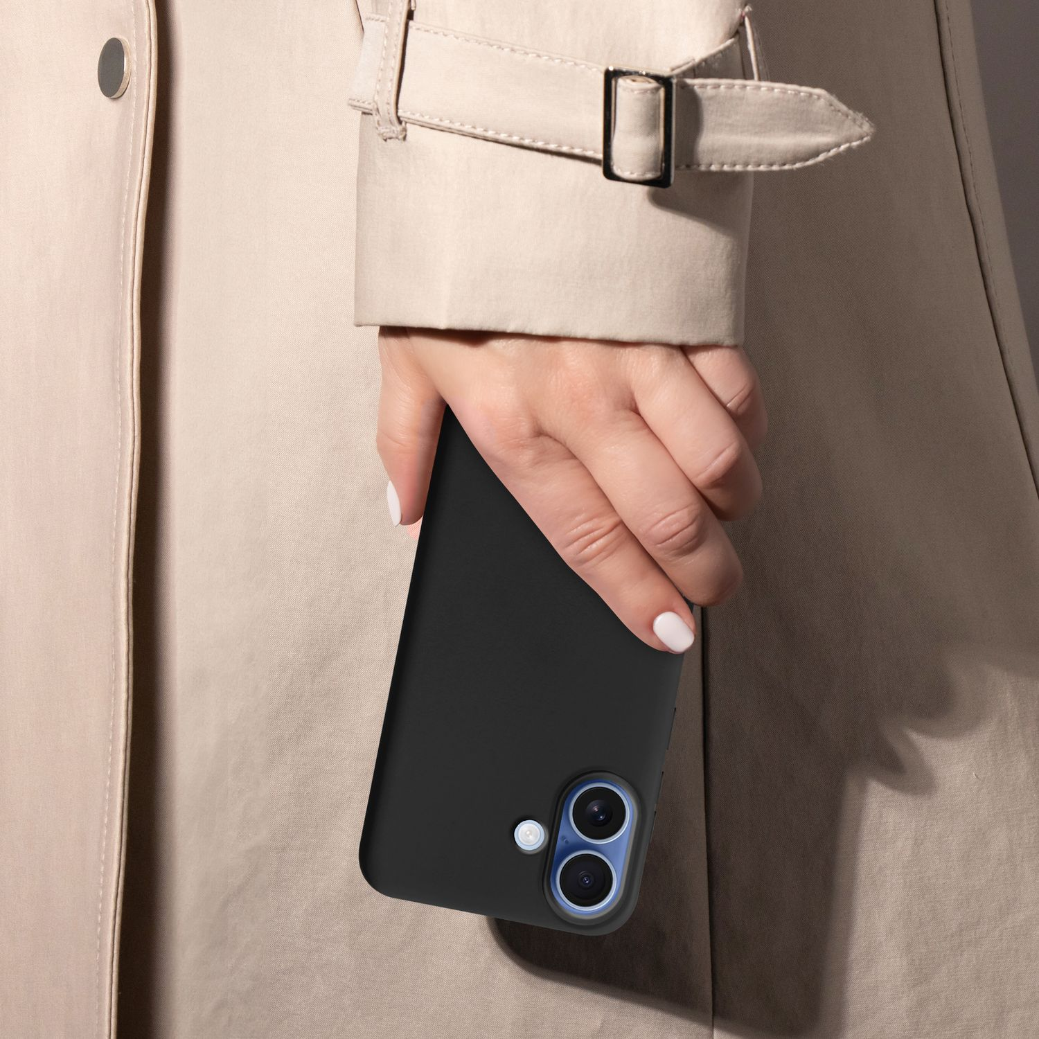 Eine Person hält ein schwarzes Smartphone und trägt einen beigefarbenen Trenchcoat. Die Hand ist mit weißem Nagellack sichtbar.