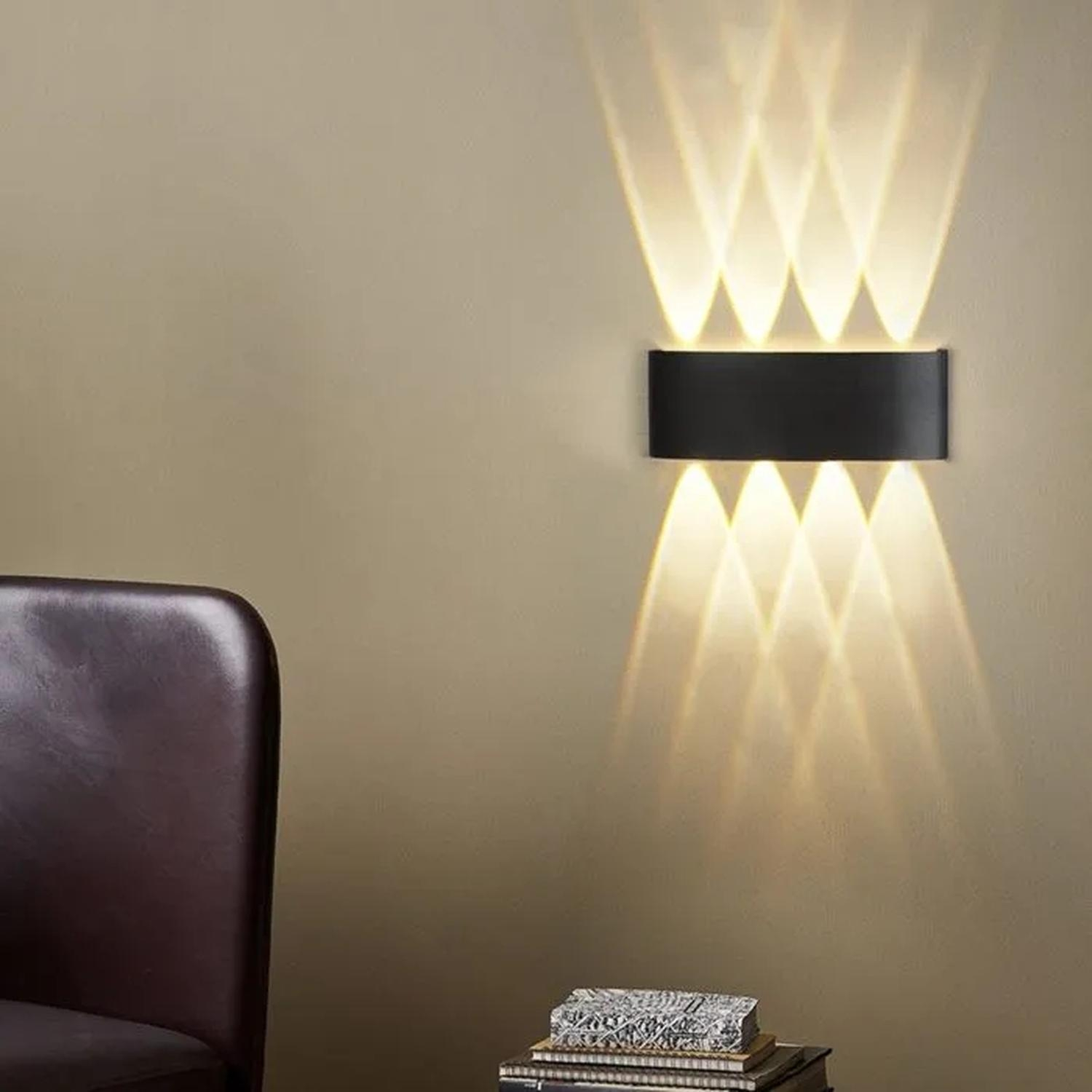 Una lámpara de pared moderna con haces de luz en una pared beige. Una silla y libros en primer plano.