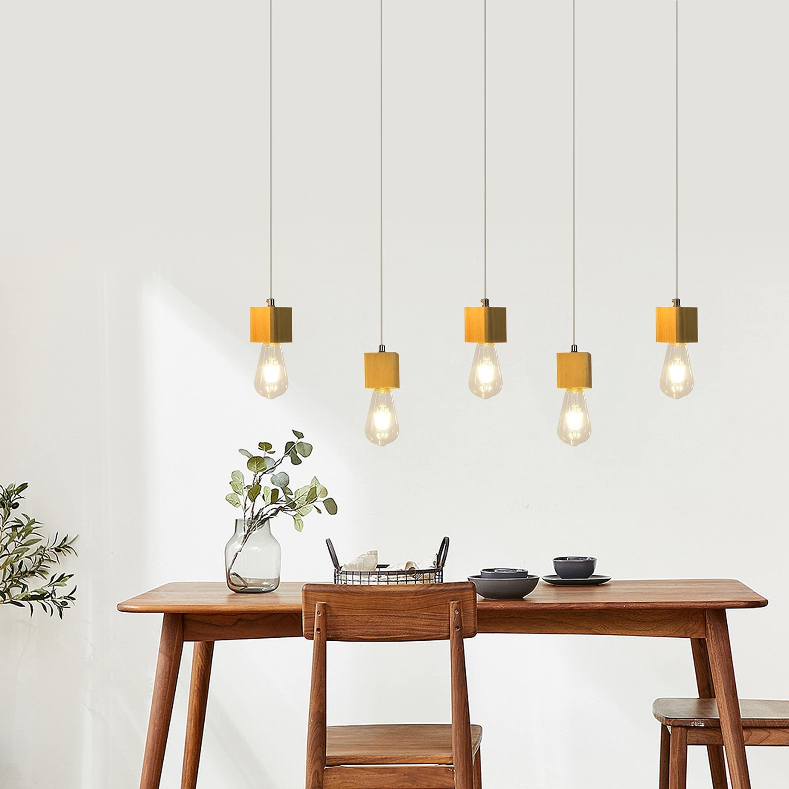 Esszimmer mit Holztisch, Stühlen und Hängelampen. Eine Vase mit Pflanzen steht auf dem Tisch. Weiße Wand.