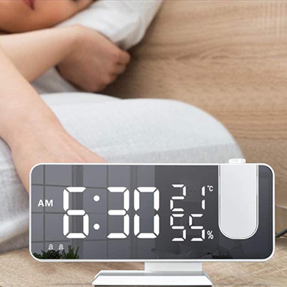 Eine Digitaluhr zeigt 6:30 Uhr morgens, 21 Grad Celsius, 55 % Luftfeuchtigkeit. Im Hintergrund schläft eine Person.