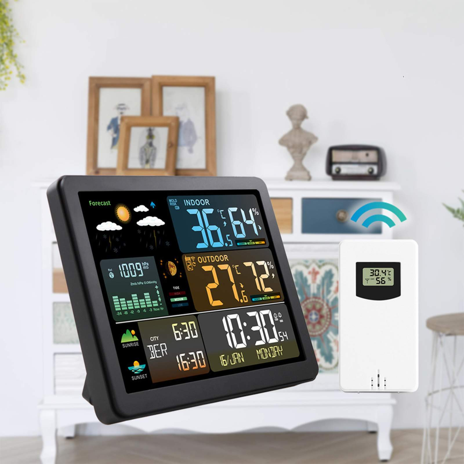 Eine Wetterstation zeigt Temperatur, Luftfeuchtigkeit und Vorhersage an. Eine weiße Fernbedienung zeigt ähnliche Daten. Deko-Objekte im Hintergrund.