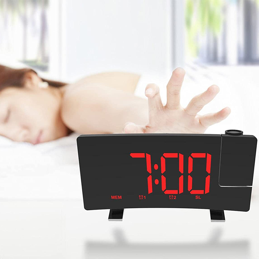 Ein schwarzer digitaler Wecker zeigt 7:00 Uhr an. Eine Person greift nach der Uhr. Der Hintergrund zeigt eine verschwommene Schlafzene.