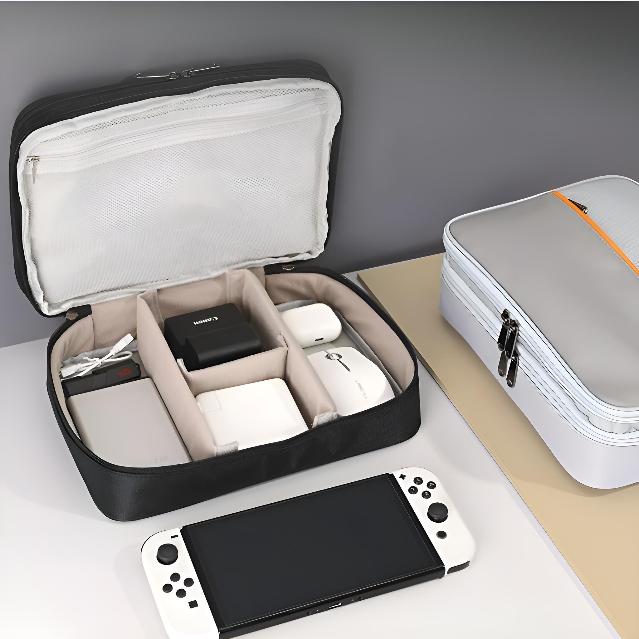 Geöffnete schwarze Tech-Tasche mit Elektronik. Eine Nintendo Switch, eine graue Tasche und eine weiße Oberfläche sind vorhanden.