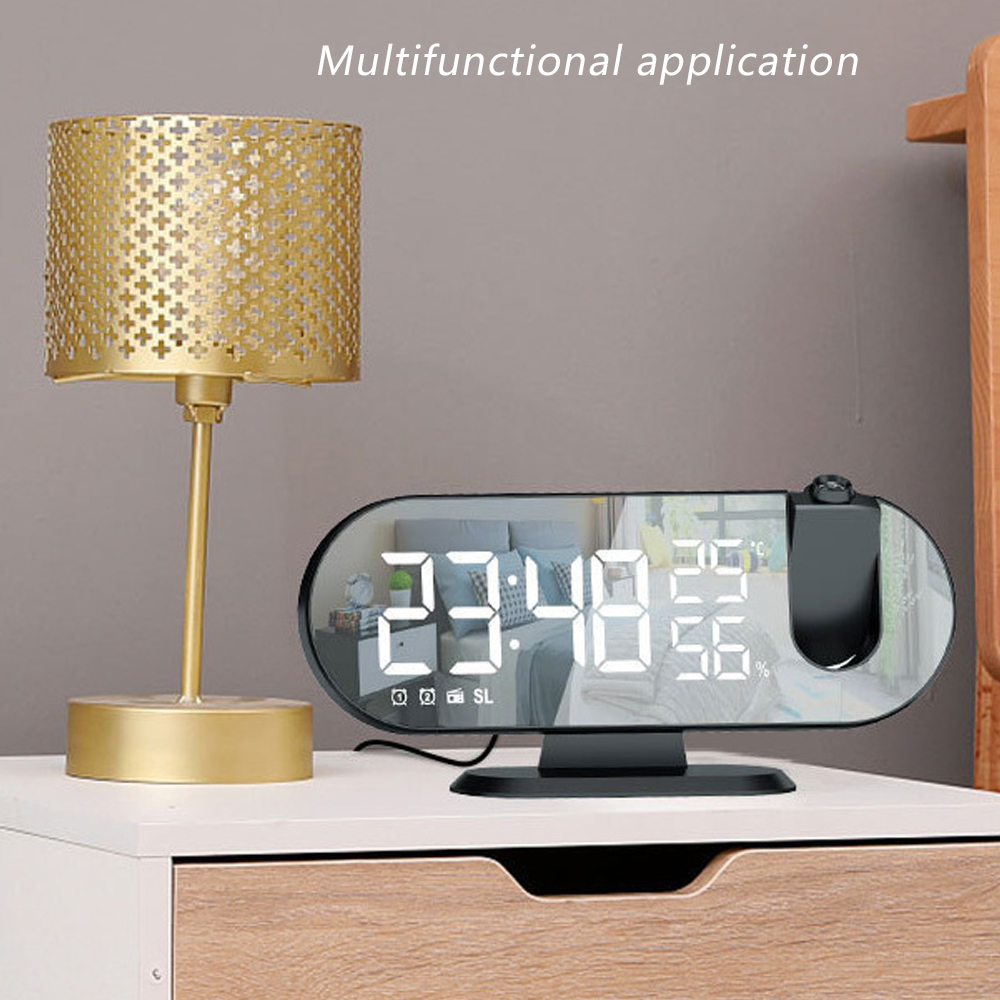 Eine goldene Lampe und eine Digitaluhr mit Uhrzeit, Temperatur und Luftfeuchtigkeit auf einer weißen Schublade. Der Hintergrund ist grau.