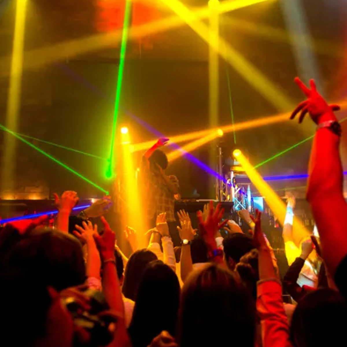 Eine Menschenmenge bei einem Konzert mit erhobenen Händen. Bühnenlichter schaffen eine farbenfrohe Atmosphäre.
