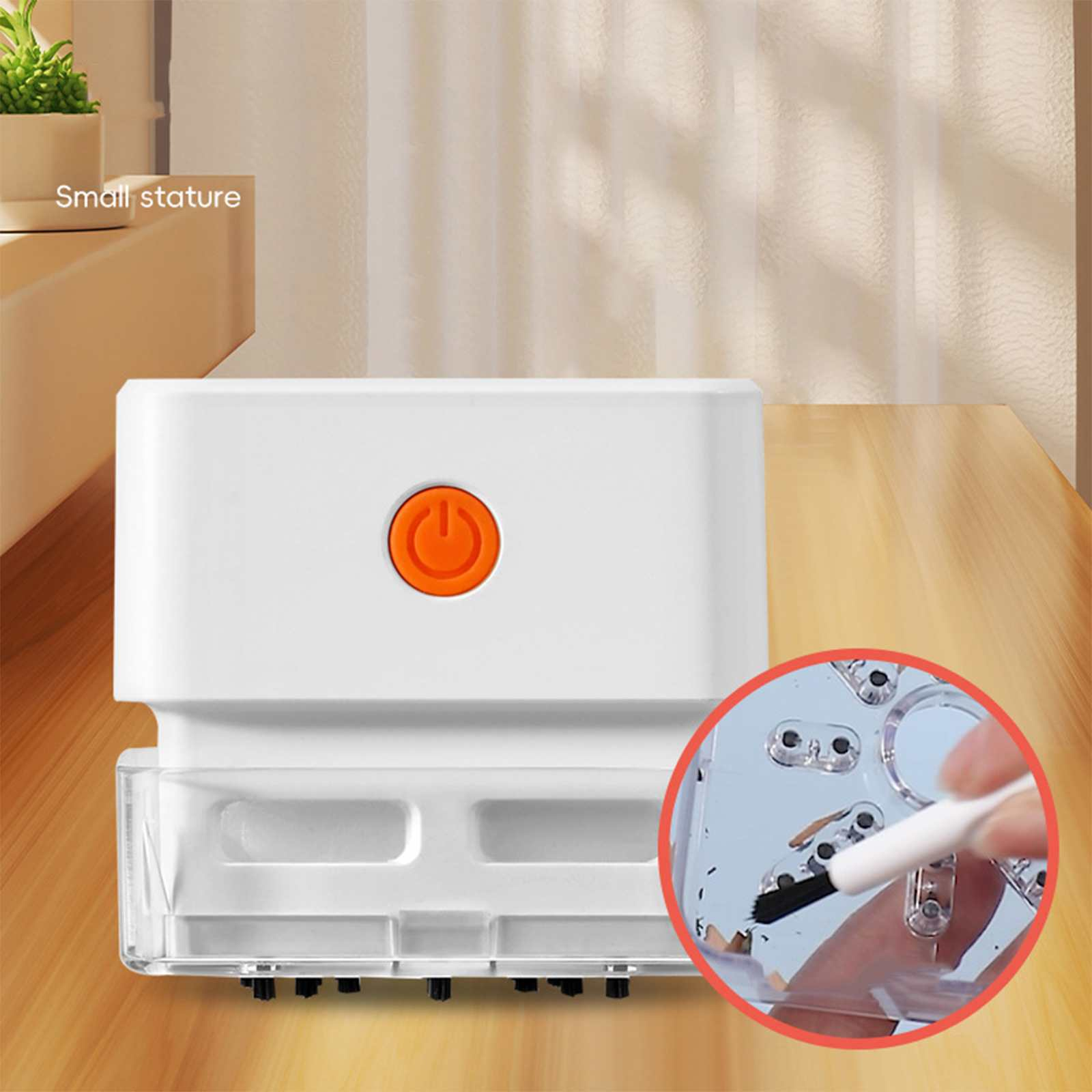 Weißes Gerät mit orangefarbener Power-Taste, transparentem Boden, auf Holztisch. Eine kleine Bürste reinigt das Gerät.