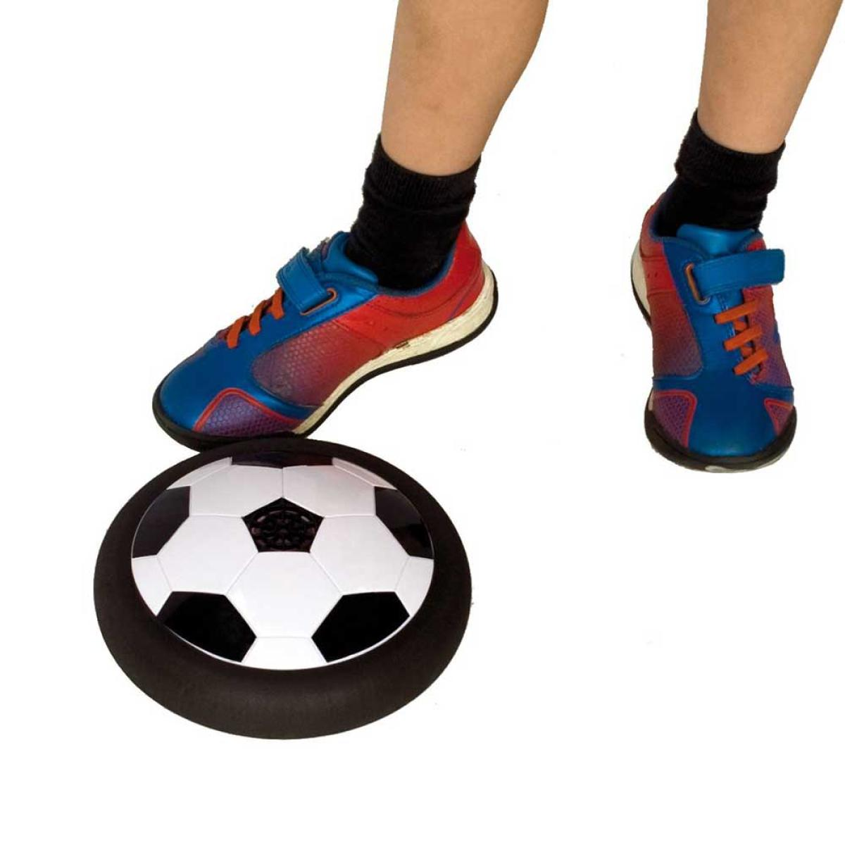 Voeten van een kind met zwarte sokken en rood/blauwe schoenen staan bij een voetbalvormige hovercraft op een witte achtergrond.
