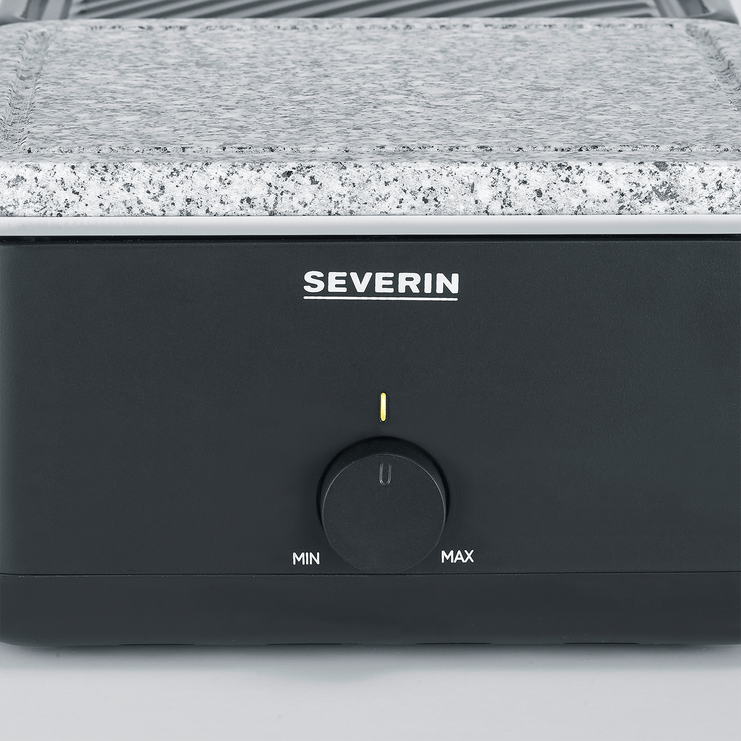 Zbliżenie czarnego grilla z szarym kamiennym blatem. Ma pokrętło z napisem 'MIN' i 'MAX' oraz nazwę marki 'SEVERIN'.