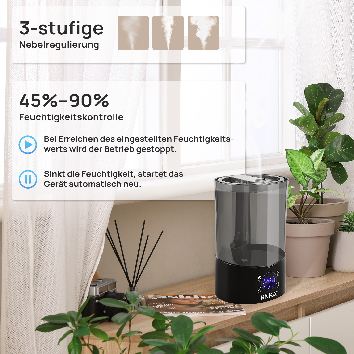 Ein Luftbefeuchter mit Digitalanzeige steht auf einer Holzoberfläche. Pflanzen und ein Fenster mit weißem Vorhang sind im Hintergrund.
