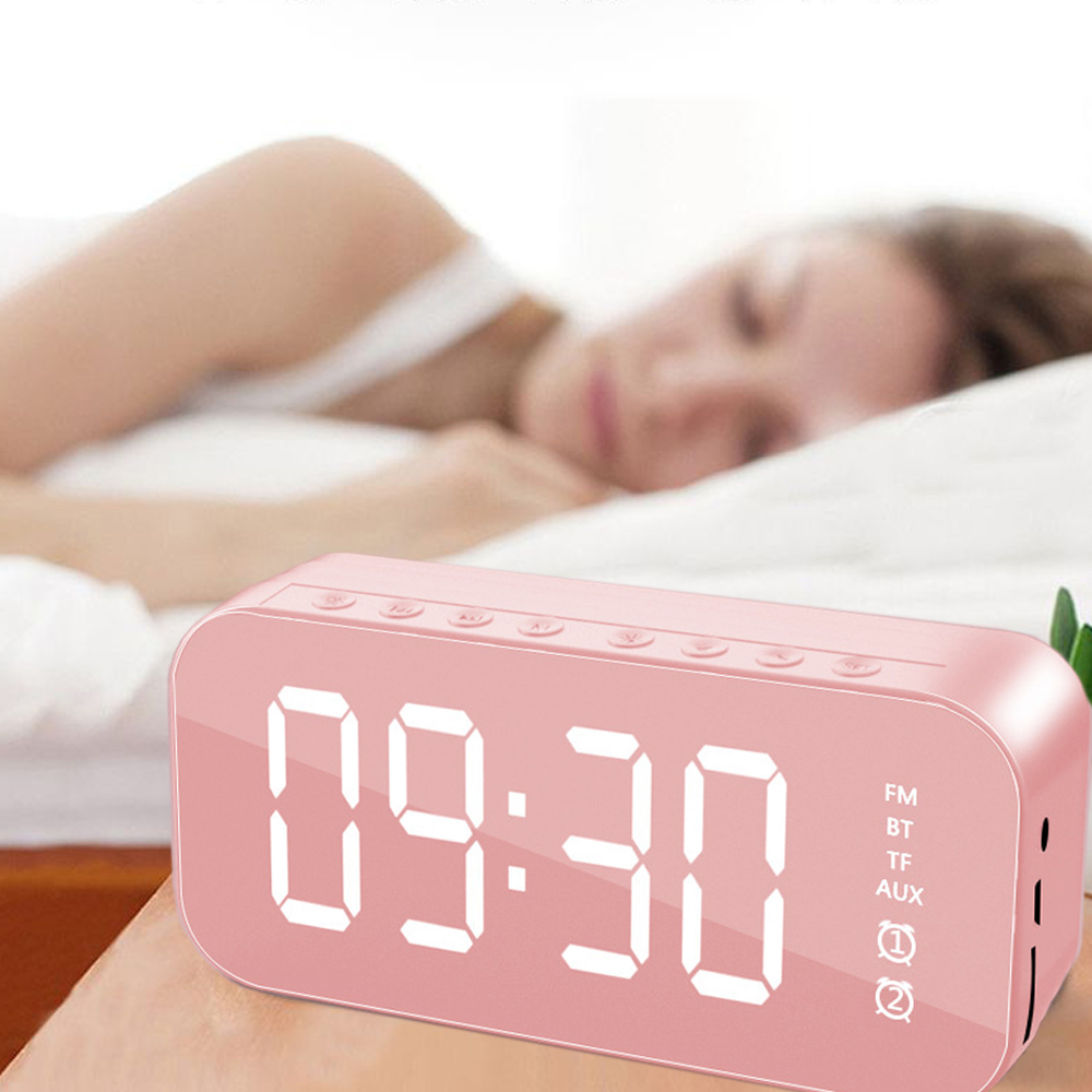 Ein rosa Digitalwecker zeigt 09:30 Uhr an. Im Hintergrund schläft eine Person. Die Uhr zeigt FM, BT, TF, AUX und zwei Lautsprechersymbole.