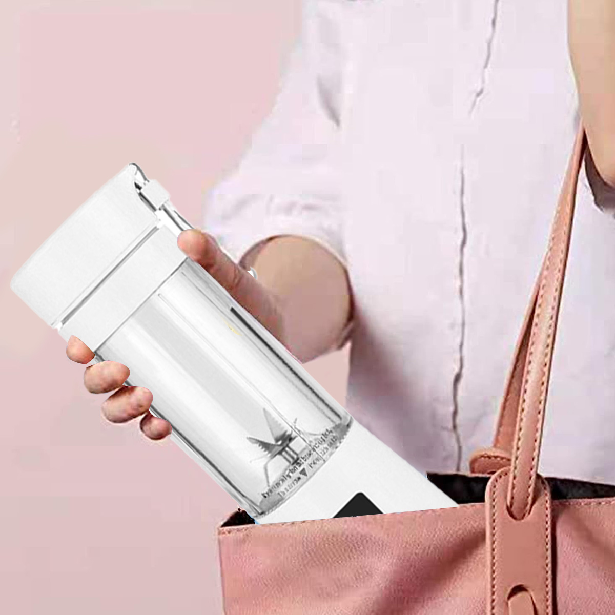 Eine Frau hält einen weißen Mixer in einer rosa Handtasche. Der Mixer ist durchsichtig und hat eine Klinge. Der Hintergrund ist ein weißes Hemd und eine rosa Wand.