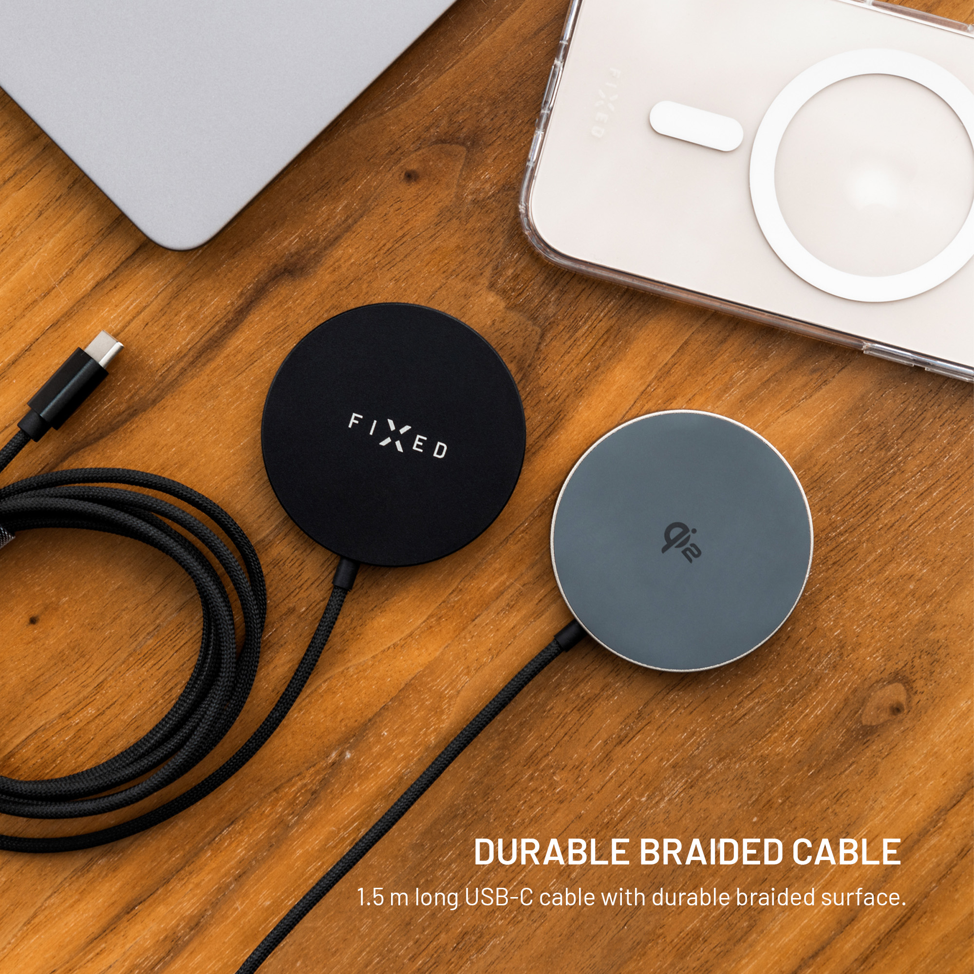 Zwei kabellose Ladegeräte, eines schwarz mit 'FIXED', eines grau mit 'qi'-Symbol, und ein Telefon auf Holzoberfläche.