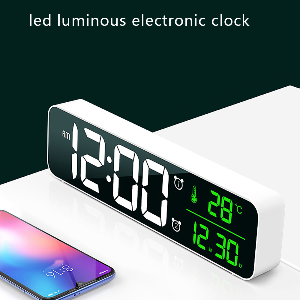 Eine weiße LED-Elektronikuhr zeigt 12:00 Uhr, 28°C und das Datum an. Im Vordergrund befindet sich ein Smartphone.