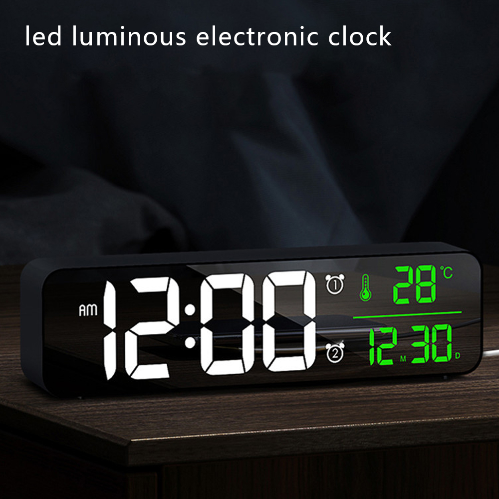 Eine elektronische Uhr zeigt 12:00 Uhr morgens und 28°C an. Die Uhr steht auf einer Holzoberfläche, mit dunklem Hintergrund.