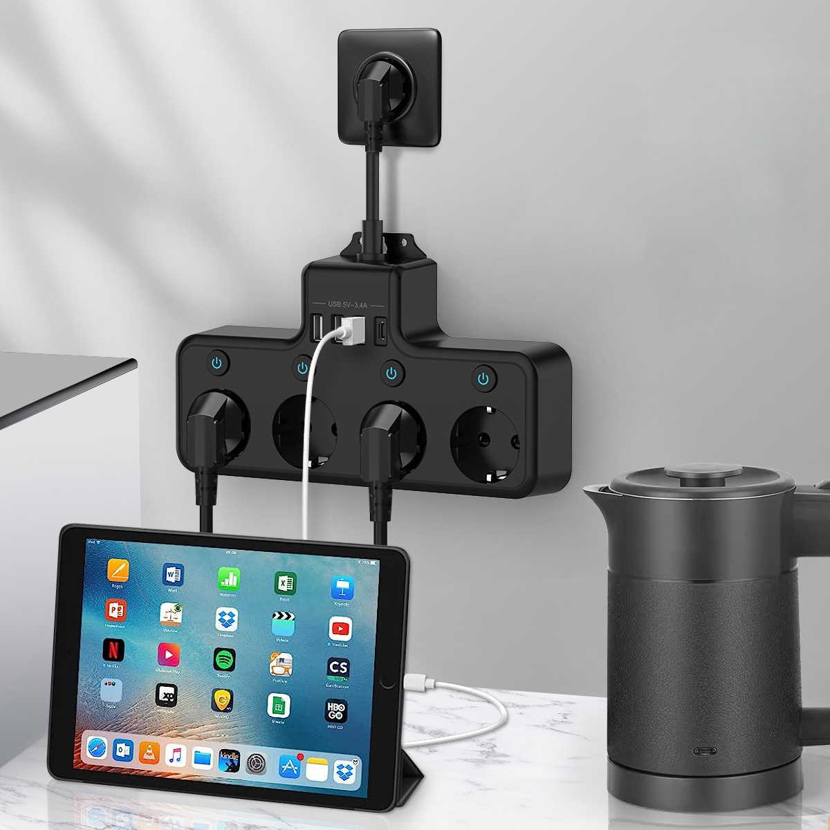 Ein schwarzer Mehrfachstecker mit mehreren Steckdosen und USB-Anschlüssen. Ein Tablet wird geladen. Rechts ist ein schwarzer Wasserkocher.