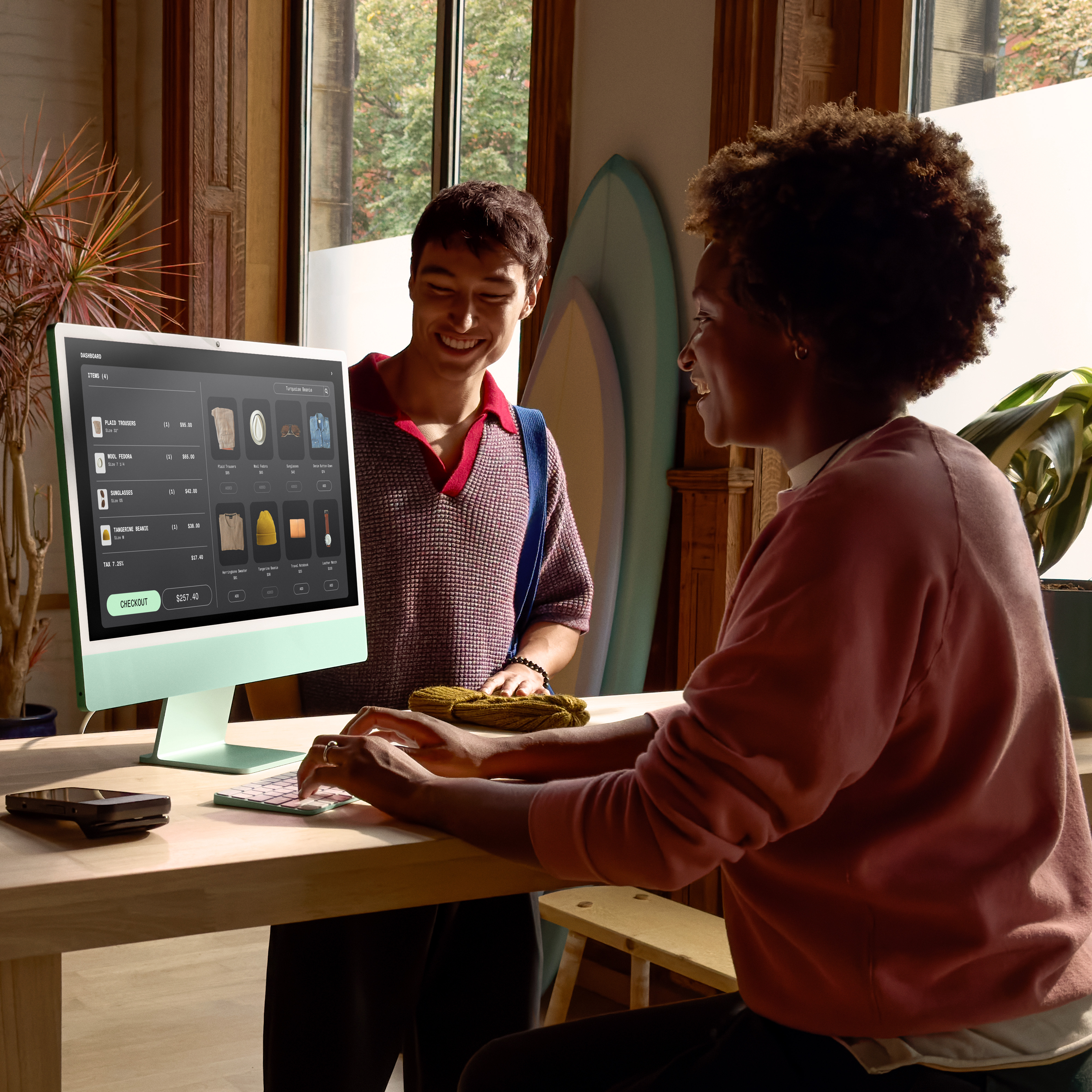 Kobieta pisze na klawiaturze, mężczyzna się uśmiecha. Ekran pokazuje produkty do kupienia. Deska surfingowa jest w tle.