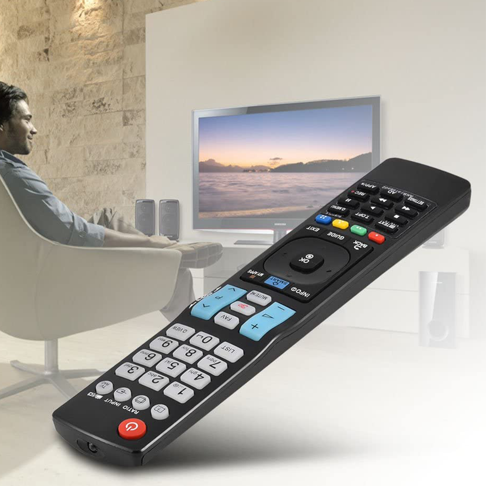 Eine schwarze TV-Fernbedienung ist im Fokus. Eine Person sitzt in einem Stuhl und schaut fern. Der Fernseher zeigt eine Landschaftsszene.