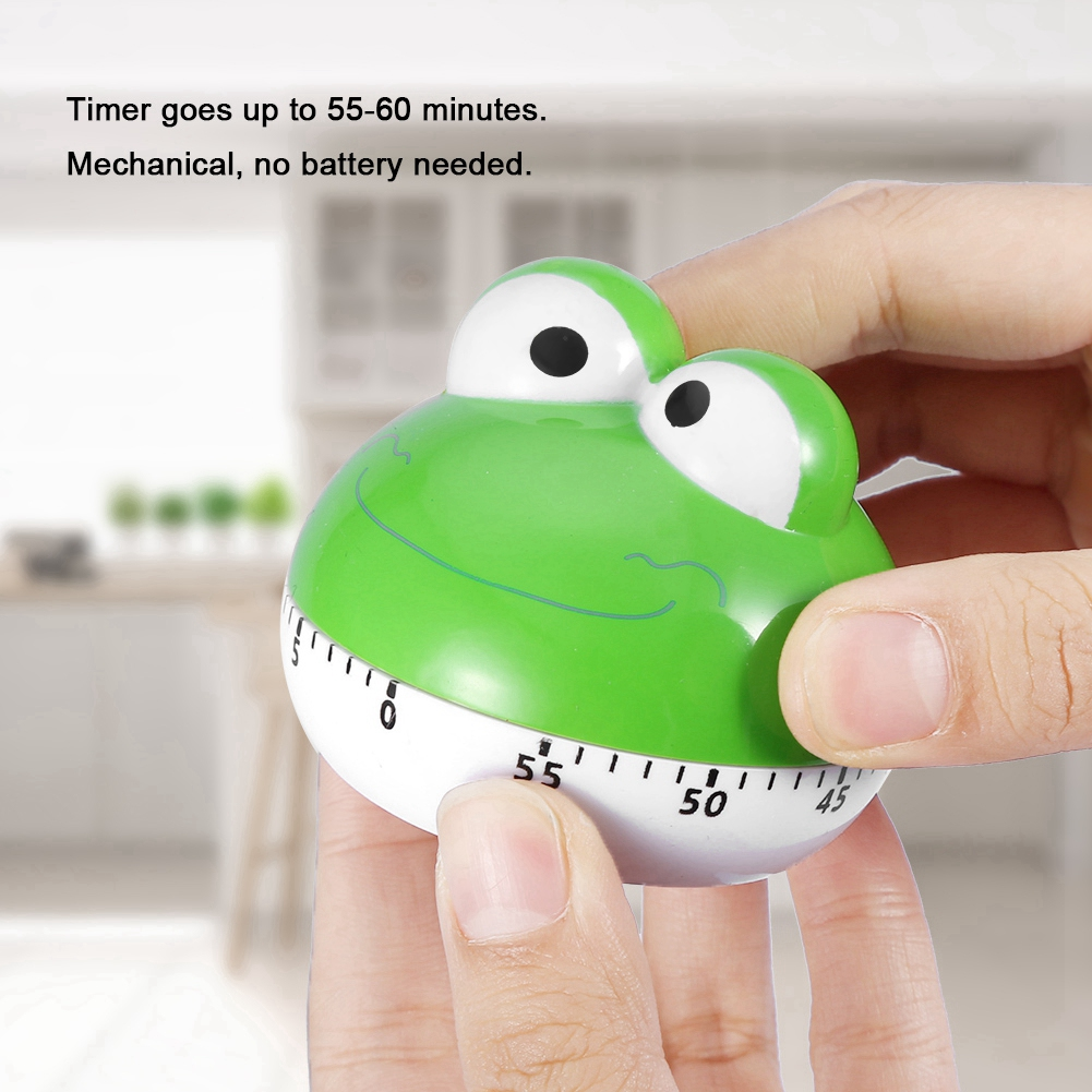 Ein grüner froschförmiger Küchentimer wird von Händen gehalten. Der Timer zeigt die Zahlen an. Hintergrund: eine verschwommene Küche.
