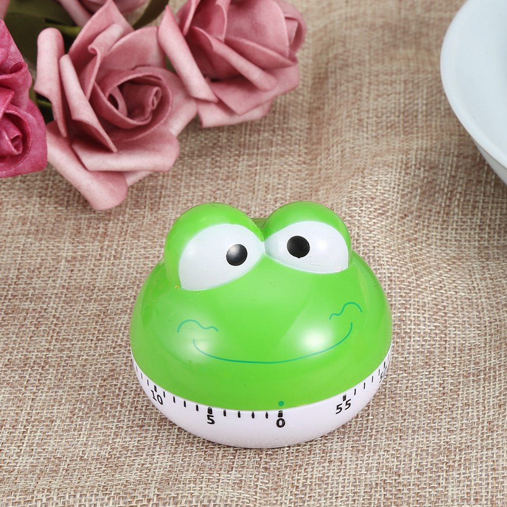 Ein grüner froschförmiger Küchentimer mit weißer Basis. Rosa Rosen im Hintergrund. Der Timer zeigt 55 Minuten.