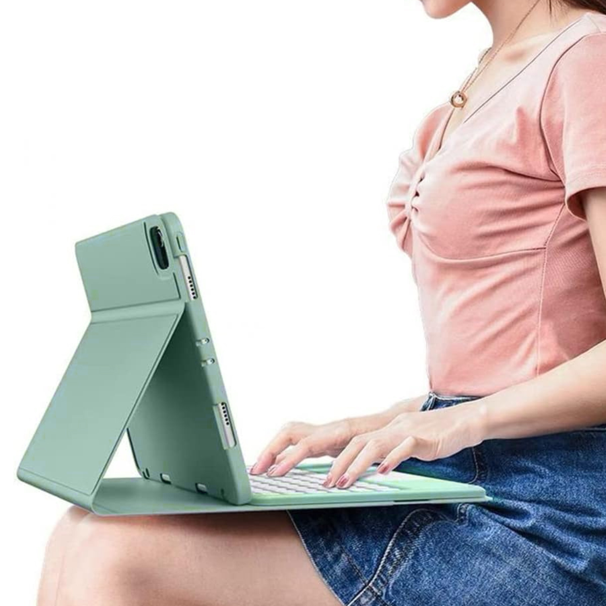 Eine Frau benutzt ein grünes Tablet mit Tastatur. Sie trägt ein rosa Hemd und Jeansshorts. Das Tablet liegt auf ihrem Schoß.