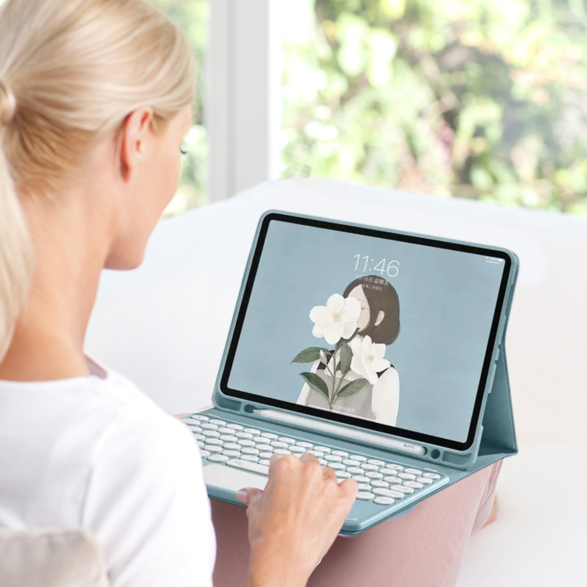 Blonde Frau benutzt ein Tablet mit Tastatur. Der Bildschirm zeigt eine Blumenillustration. Im Hintergrund ist verschwommenes Grün zu sehen.