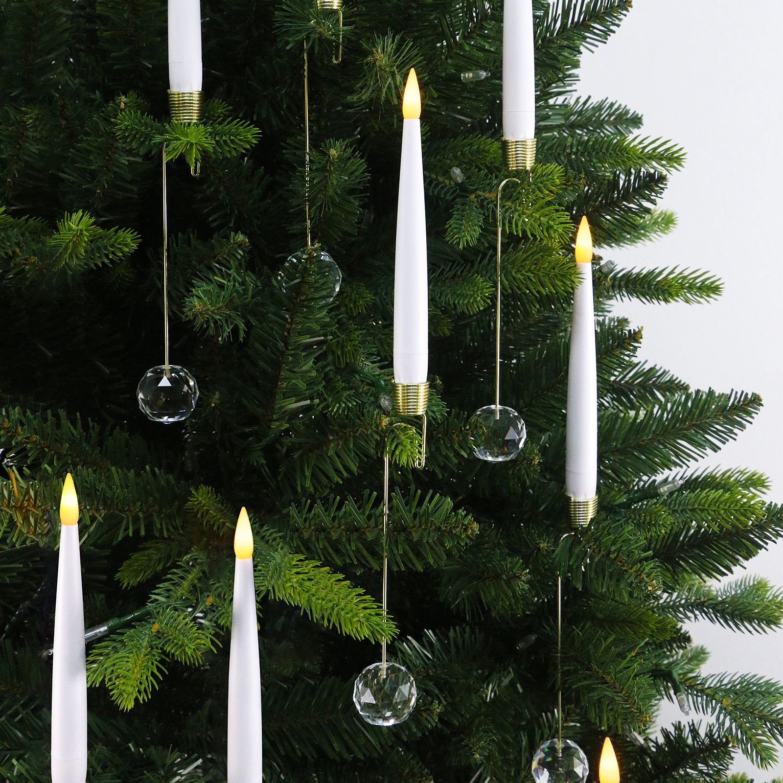 Weihnachtsbaum mit weißen Kerzenlichtern und Kristallornamenten. Grüner Baum, weiße Kerzen mit gelben Spitzen, hängende Kristallkugeln.